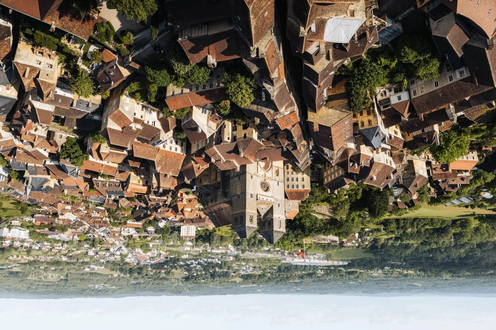 Vue aérienne d'une vieille ville avec des bâtiments en toits de tuiles, entourée de verdure et d'une rivière.