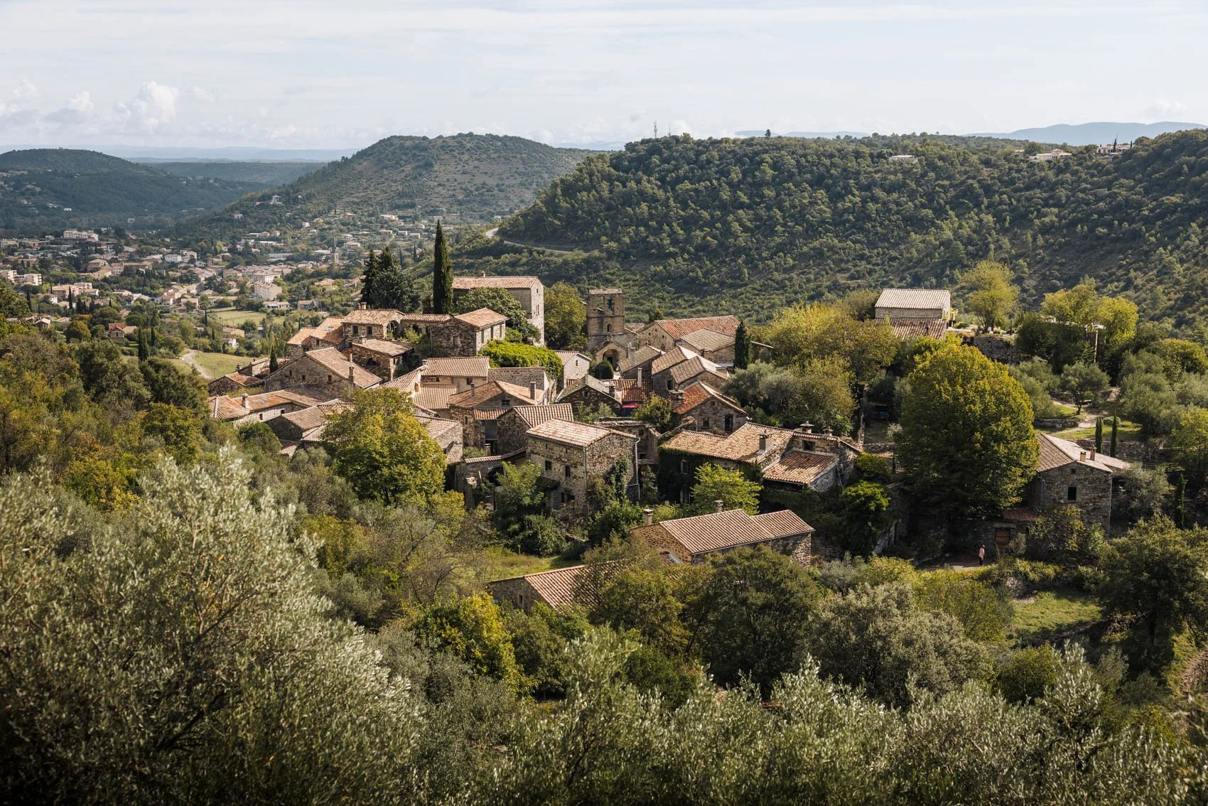 Village perché dans une région montagneuse avec des maisons en pierre, entouré de verdure et de collines boisées.