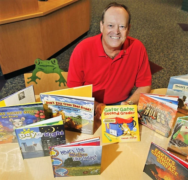 Children's book author Conrad Storad sits in the children's section of the Barberton Public Library surrounded by just a few of the fifty books he has written. Storad will be one of five people from Barberton inducted into the Barberton Walk of Fame. (Karen Schiely/Akron Beacon Journal)
