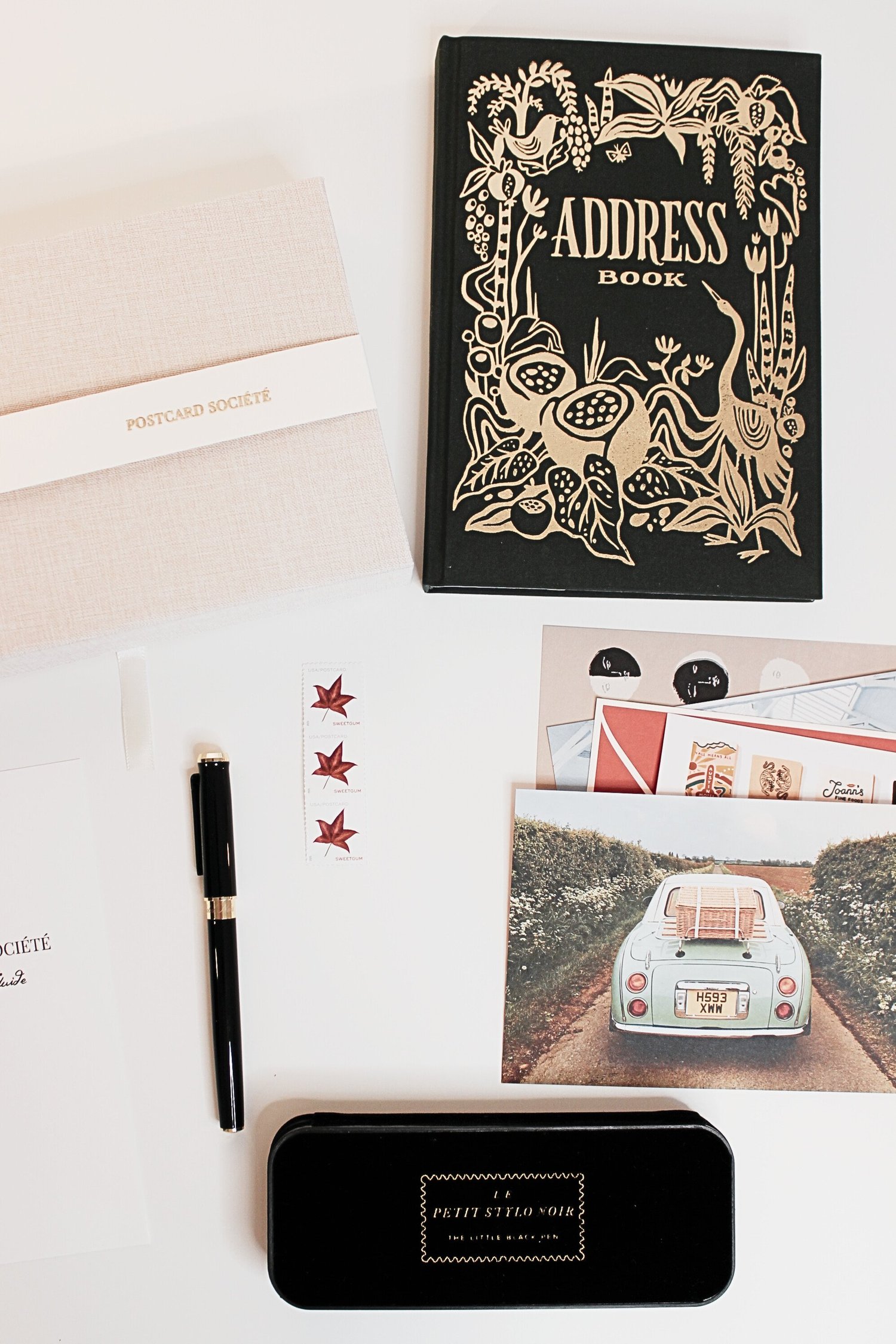 The Postcard Société founding box — postcards, fountain pen, stamps and stationery laid out on a white surface