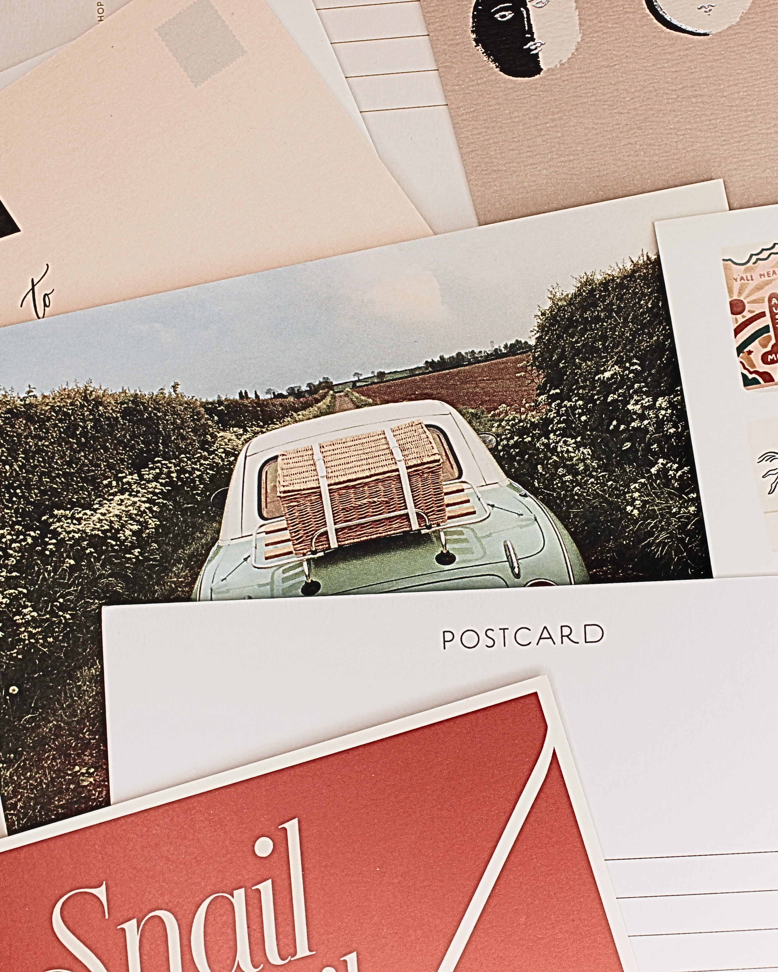 Close-up of several postcards, featuring images of landscapes and abstract art, with the word 'POSTCARD' visible on one, and decorative designs and text on others, layered in an overlapping manner.