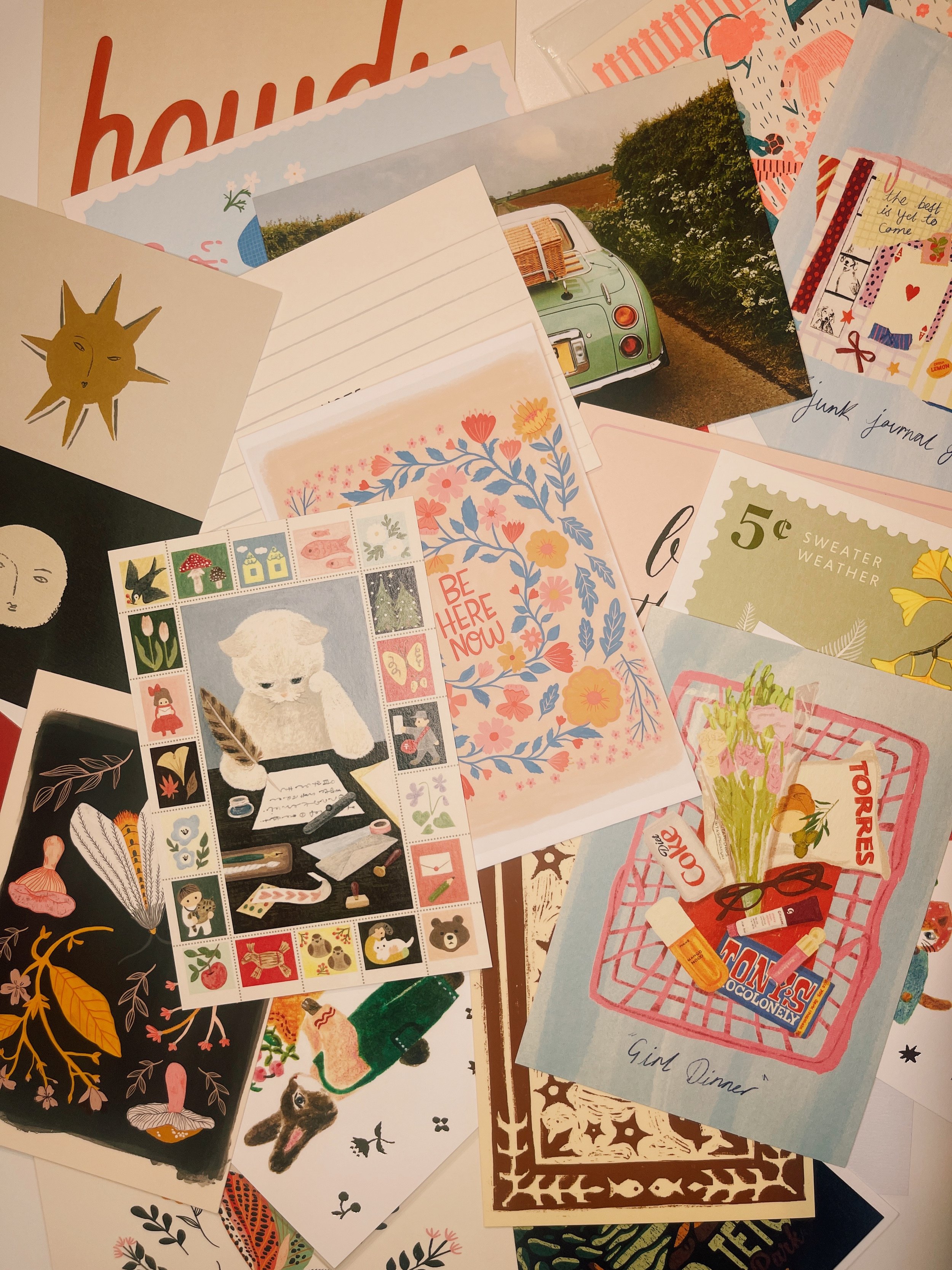 Postcards scattered on a desk, some being used for Edition 01 of The Postcard Société, postcard correspondence subscription box curated by social and cultural psychologist and travel psychologist Dr. Katie Blake, PhD.