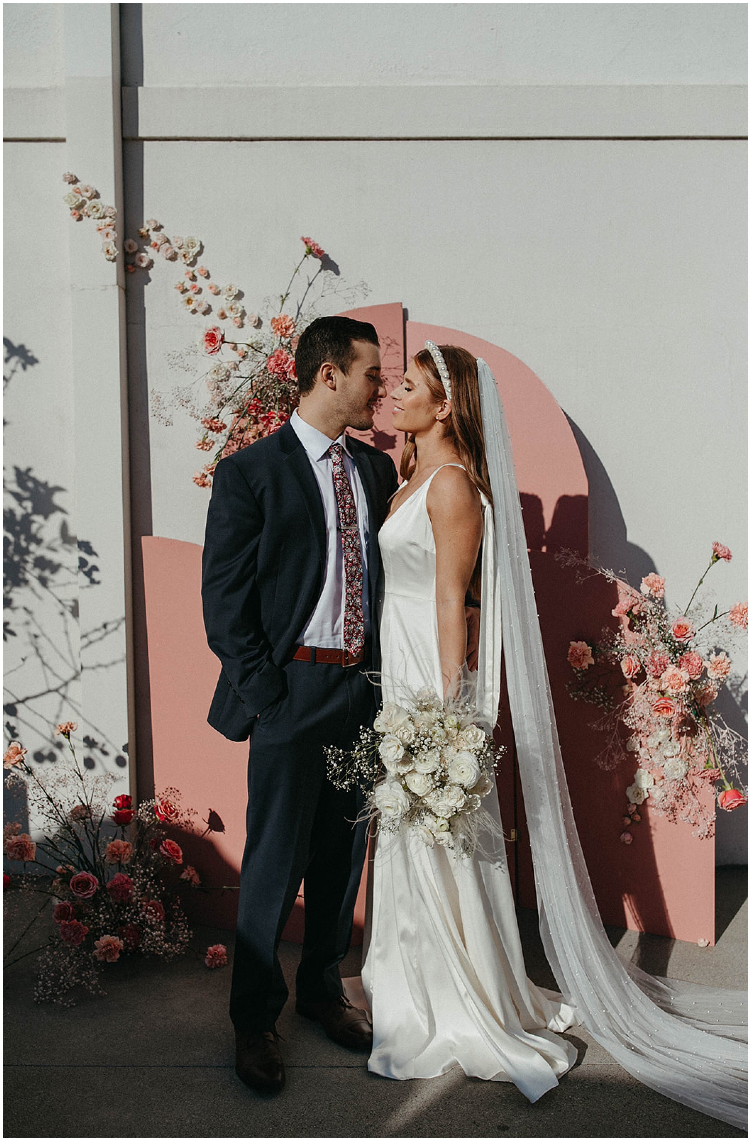 bride and groom standing in front of pink arch