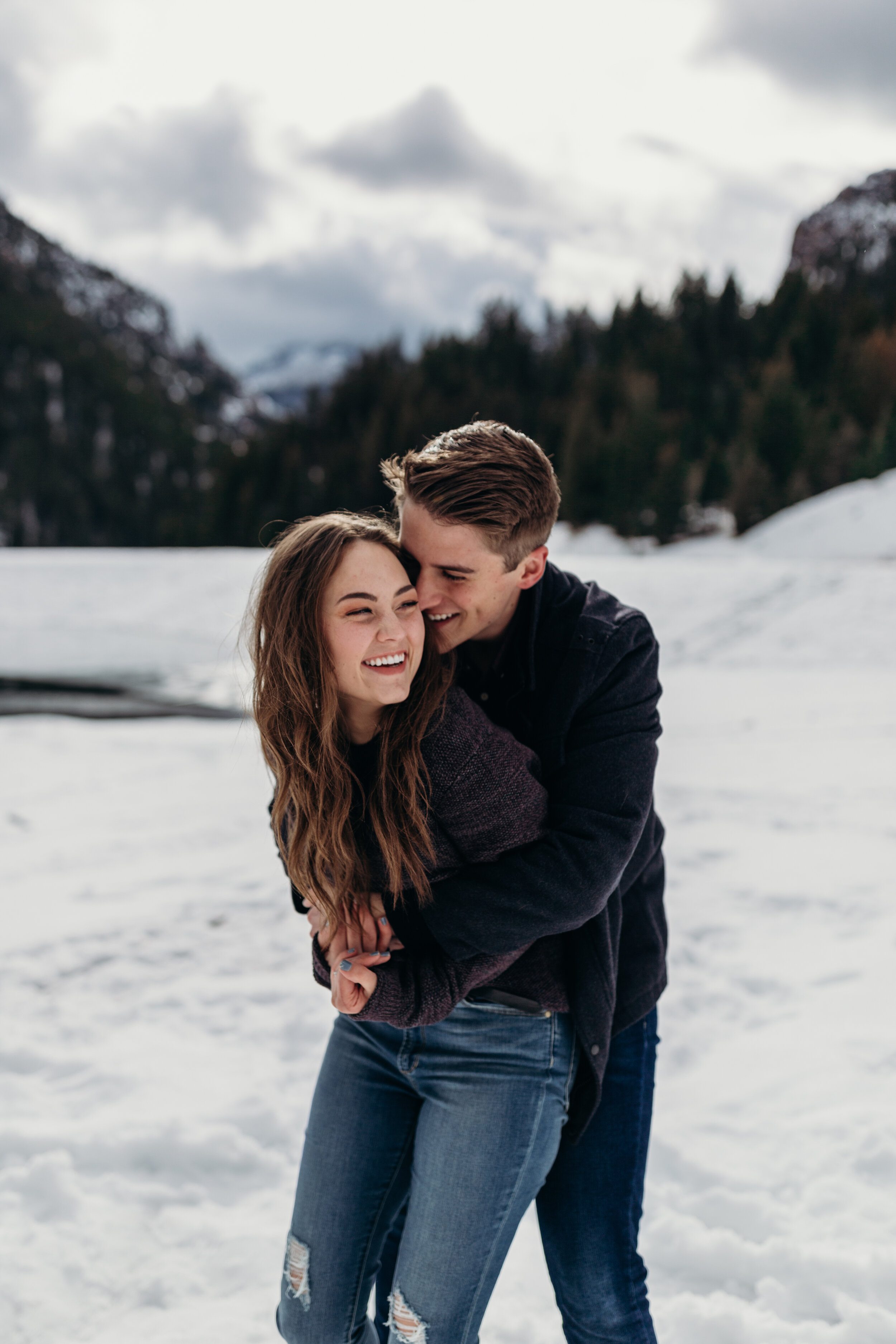 Snowy winter mountain engagements windy hair ice lake pine trees laughing couple shoot #coupleshoot #utahphotographer #weddingphotographer #engagements #engagementshoot #winterengagements