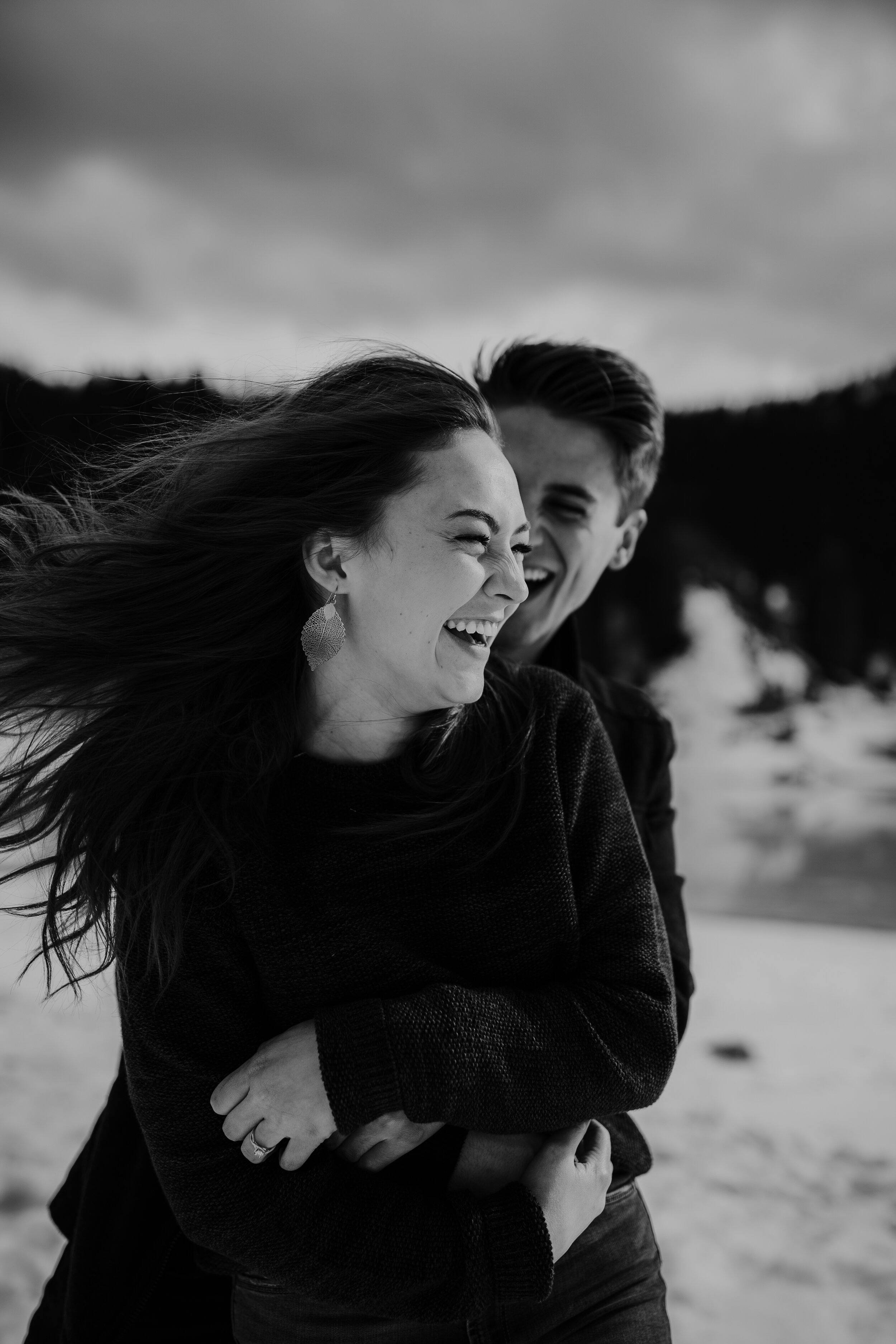 Adventurous playful snowy winter mountain engagements windy hair pine trees laughing couple shoot #coupleshoot #utahphotographer #weddingphotographer #engagements #engagementshoot #winterengagements