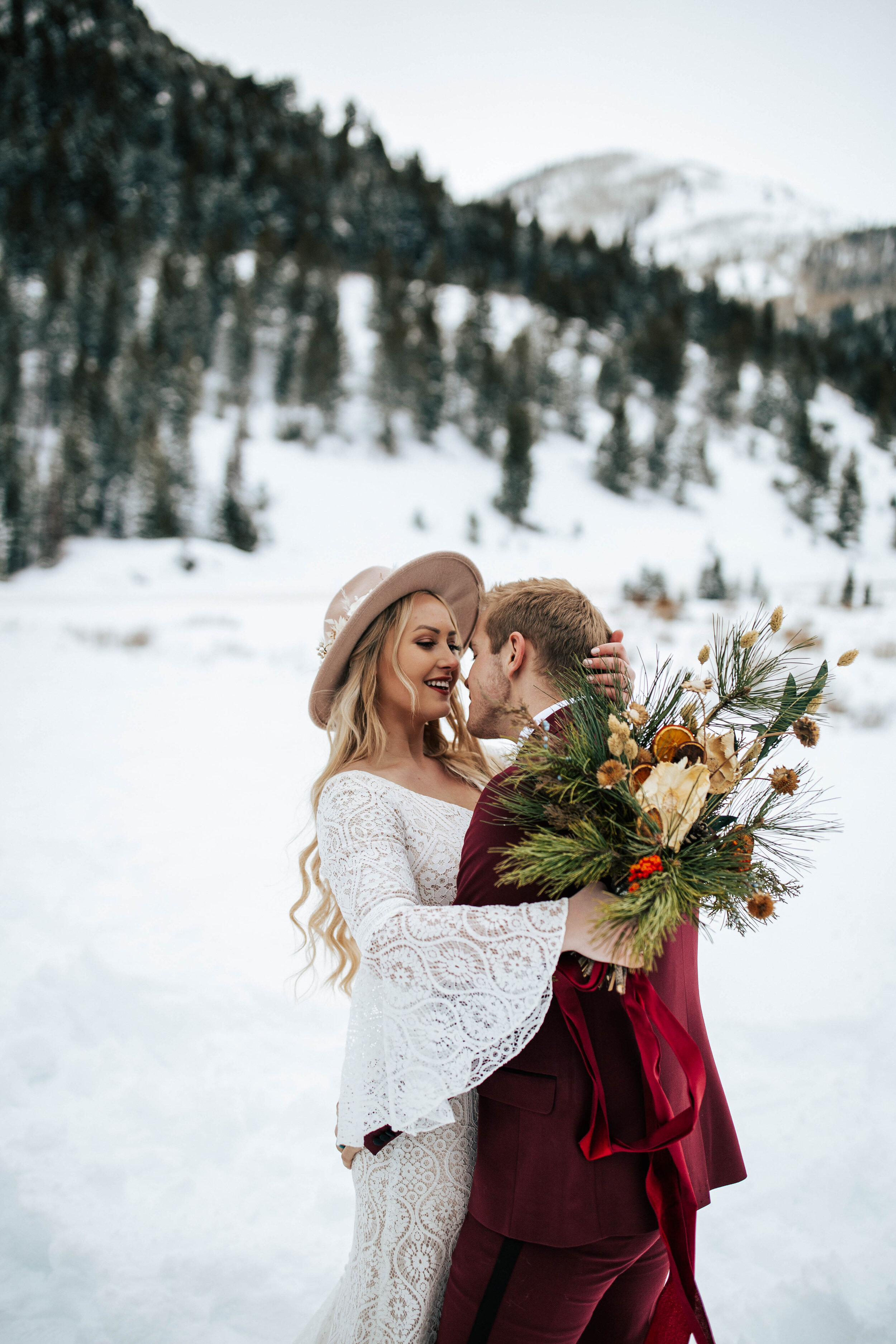 Snowy winter mountain bridal shoot bride and groom maroon suit bouquet pine trees Utah mountain wedding elopement photographer #utahphotographer #weddingphotographer #elopement #elopementphotographer