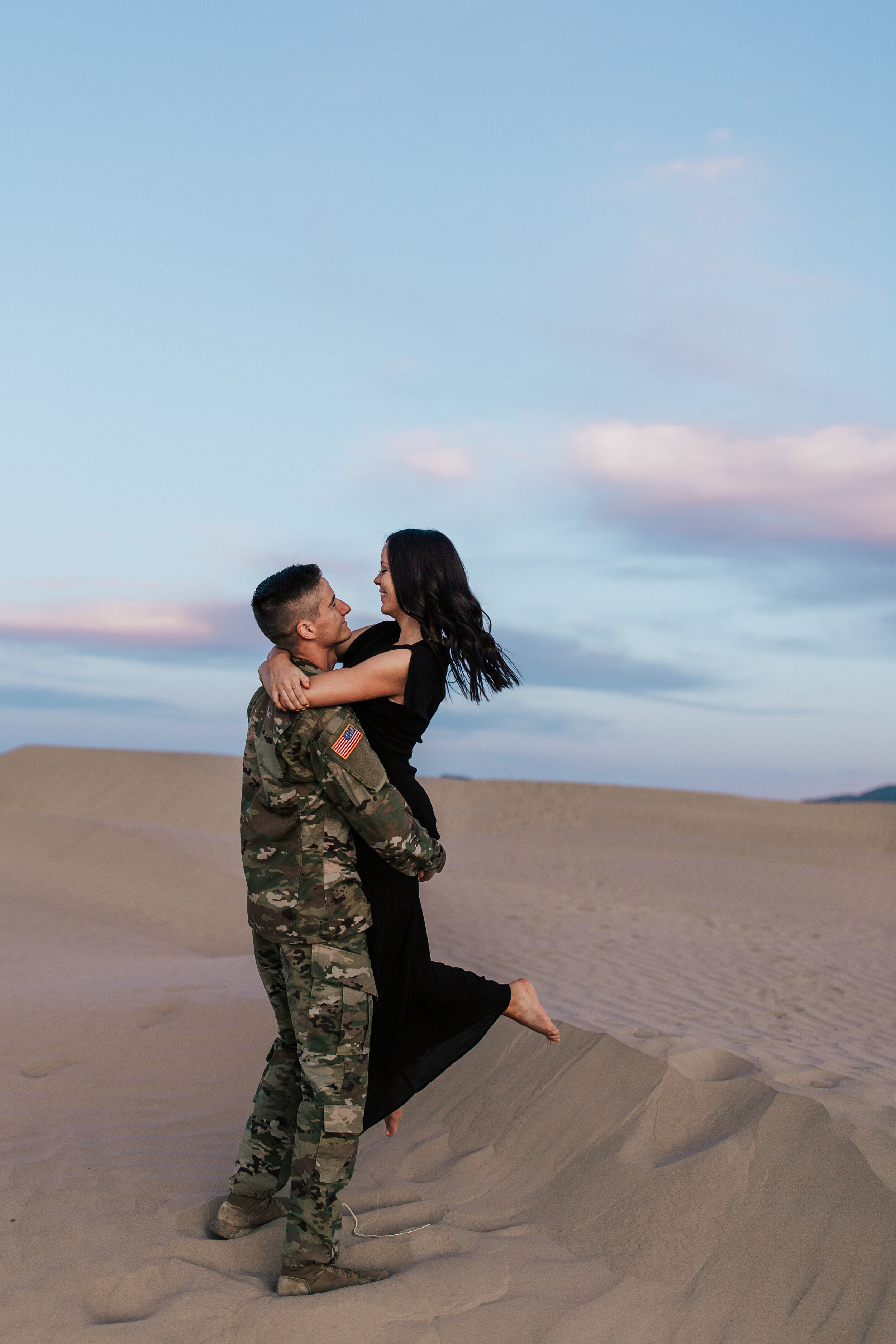 Romantic windy sand dunes engagement session couple shoot long black flowy dress military uniform adventurous desert shoot couple running #engagements #photographer #weddingphotographer 