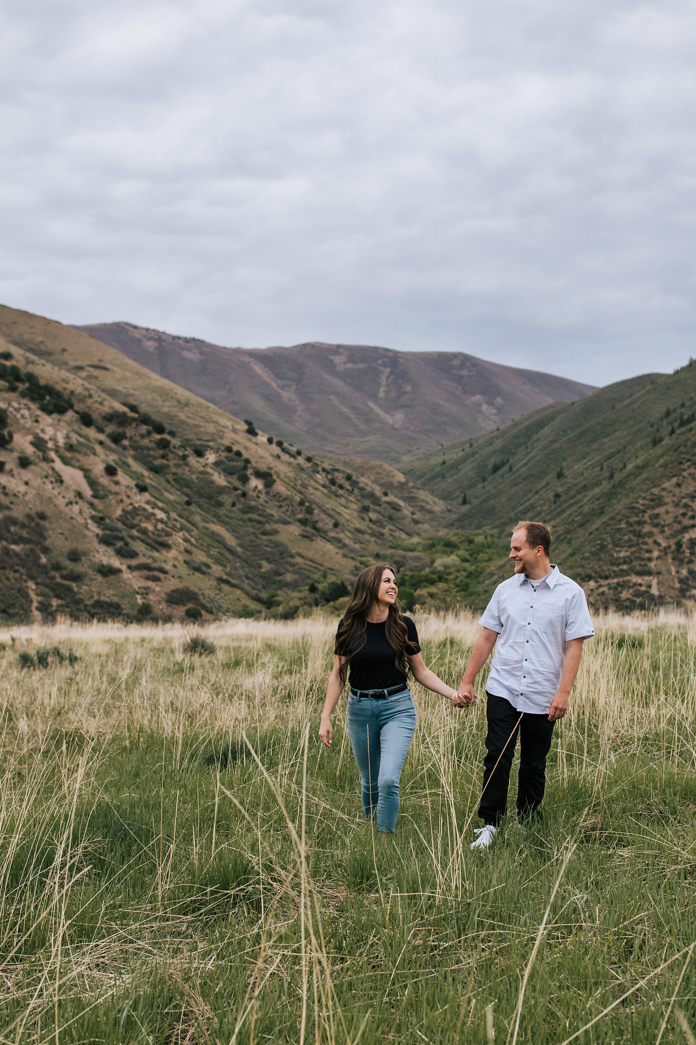  A beautiful couple walk through a grassy field in the mountains in a stunning honeymoon styled couples shoot by Emily Jenkins Photography. Couple goals walking couple pose inspiration ideas and goals client attire inspiration outdoor photo shoot loc