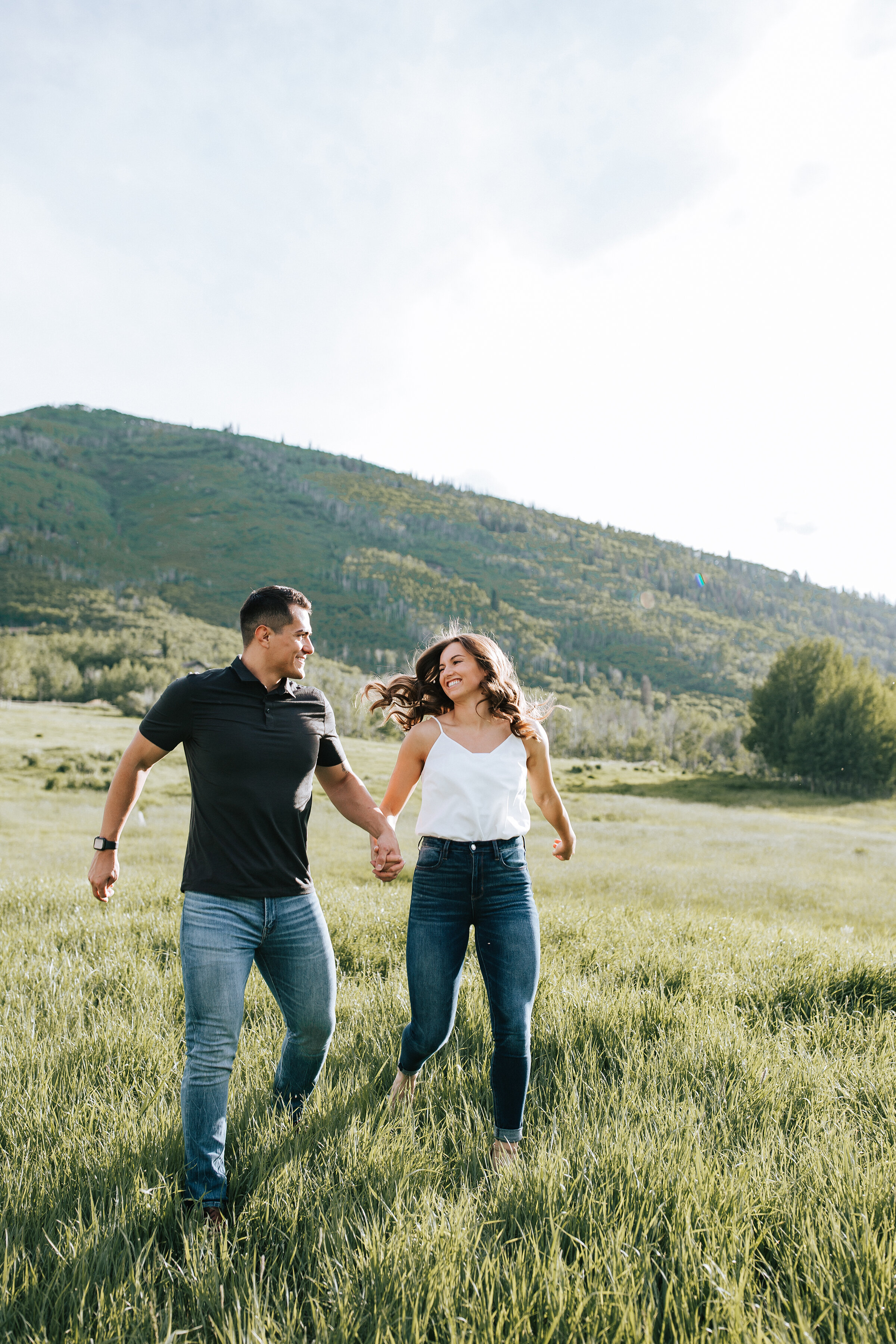  A newly wed couple run through a grassy hill top in a beautiful bright honeymoon couples photo shoot. Casual client attire for a honeymoon photo shoot photo shoot inspiration ideas and goals couple goals couple pose inspiration ideas and goals outdo