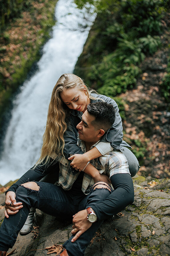  Stunning newlyweds hold each other as they sit by a beautiful waterfall in a honeymoon styled couples shoot by professional photographer Emily Jenkins Photography. Sitting couples pose inspiration ideas and goals casual client attire inspiration out