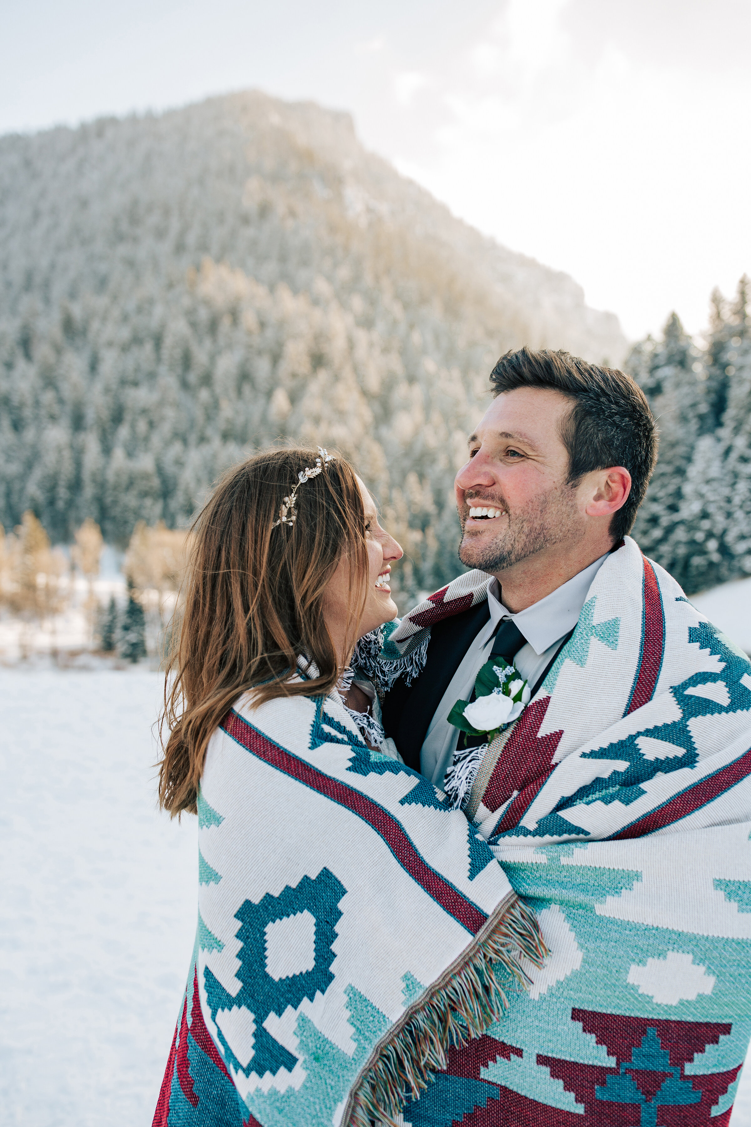  A couple cuddle together in a blanket in the snow dusted mountains on their honeymoon. Professional honeymoon photographer Emily Jenkins Photography outdoor winter photography inspiration ideas and goals couple pose inspiration winter couple pose co