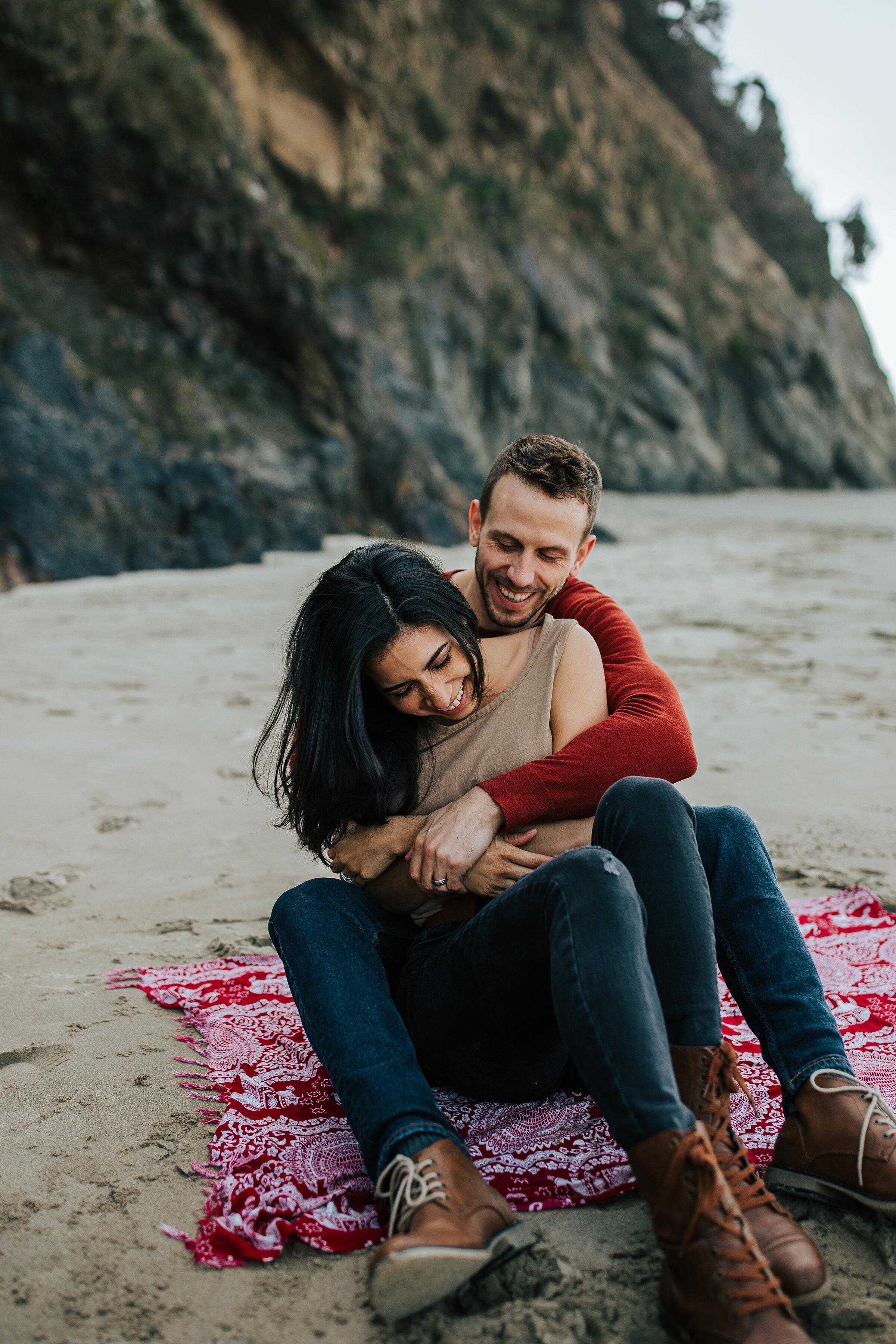  A happy couple hold each other as they sit on a rose petal covered beach in a beautiful honeymoon couples shoot by professional photographer Emily Jenkins Photography. Couple goals couple sitting pose inspiration  honeymoon location inspiration idea