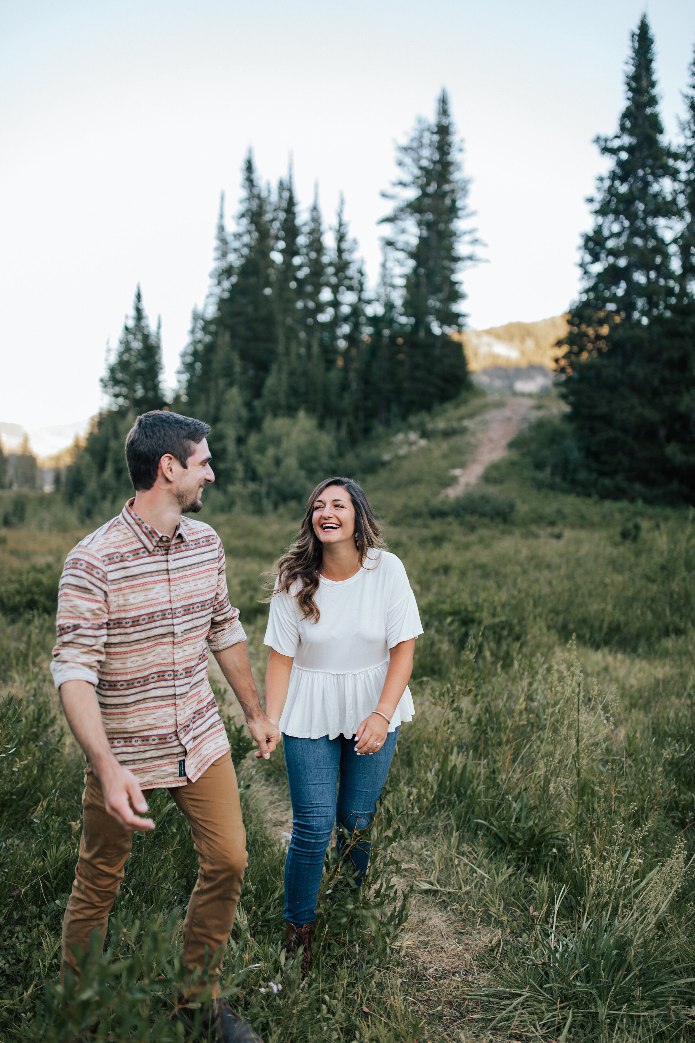  A couple giggle together and they walk through the wooded area in a beautiful engagement session by Emily Jenkins Photography. Professional Utah engagement photographer couple goals client attire inspiration casual engagement attire inspiration outd