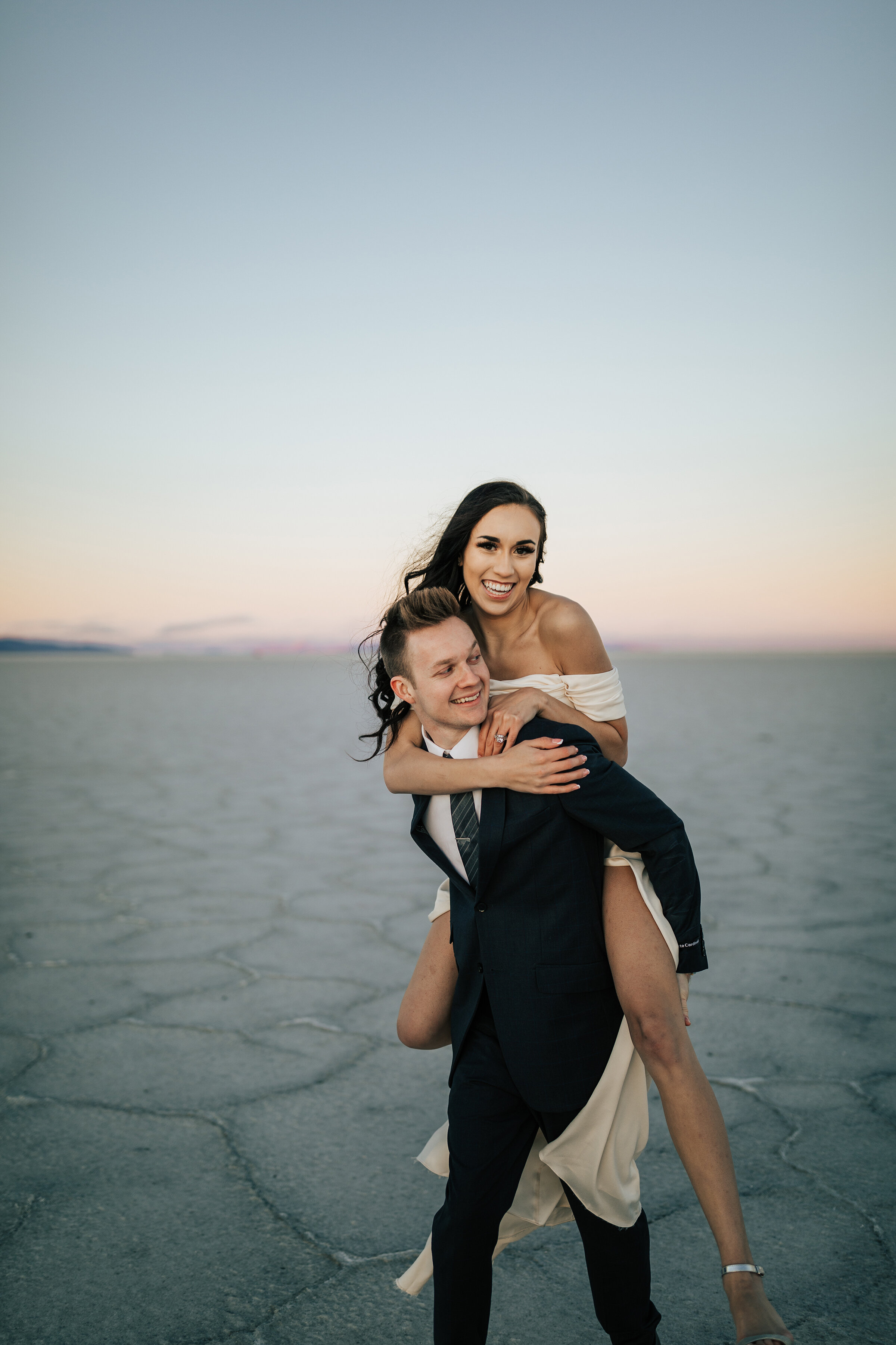  A playful groom gives his bride a piggy back ride in a beautiful hazy elopement styled photo shoot in the Utah desert. Professional Utah photographer Emily Jenkins Photography couple goals playful couple pose inspiration outdoor photo shoot goals id