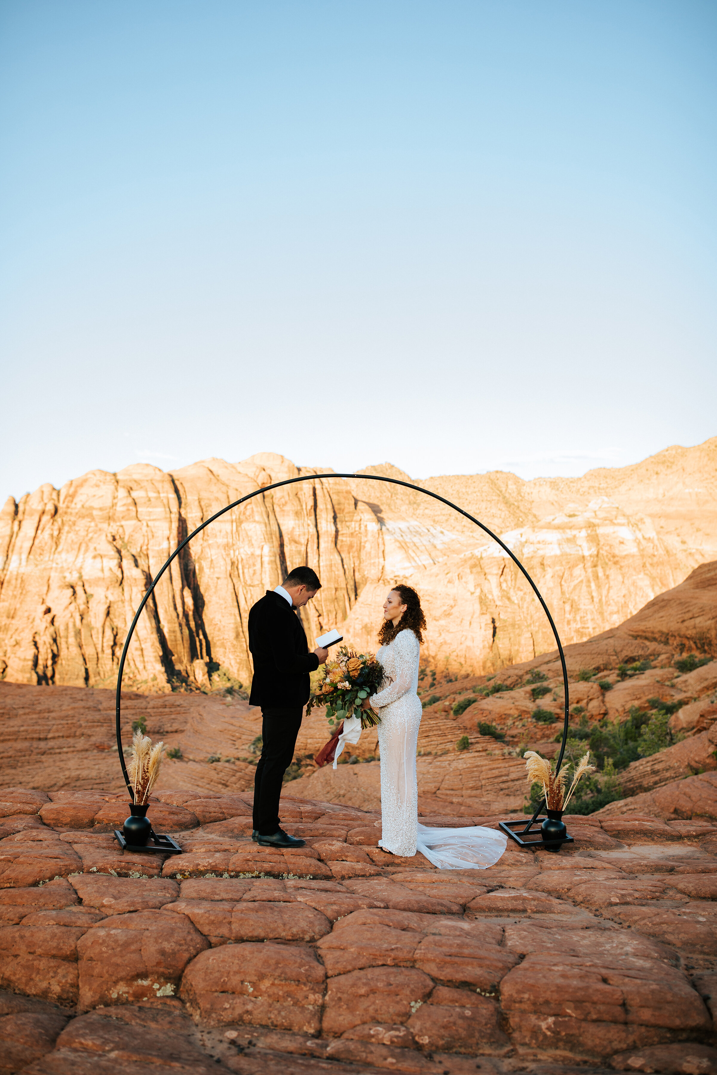  A beautiful couple exchange rings under a stunning circle arch in the Utah desert in a beautiful elopement styled photo shoot by professional Utah photographer Emily Jenkins Photography. Wedding arch inspiration ideas and goals outdoor wedding cerem