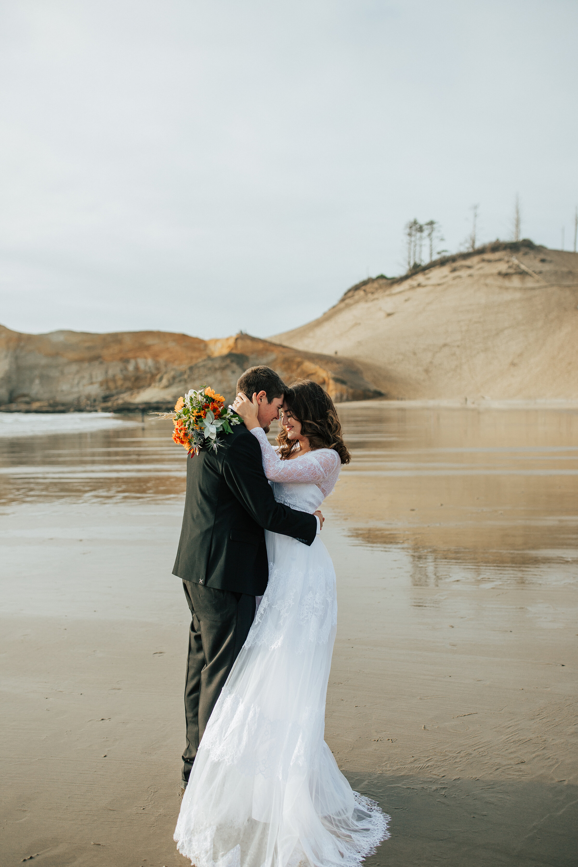  A beautiful couple share a romantic moment on the beach of the Oregon Coast by Emily Jenkins Photography. Wedding bouquet inspiration ideas and goals long sleeved wedding dress inspiration ideas and goals professional elopement photographer location