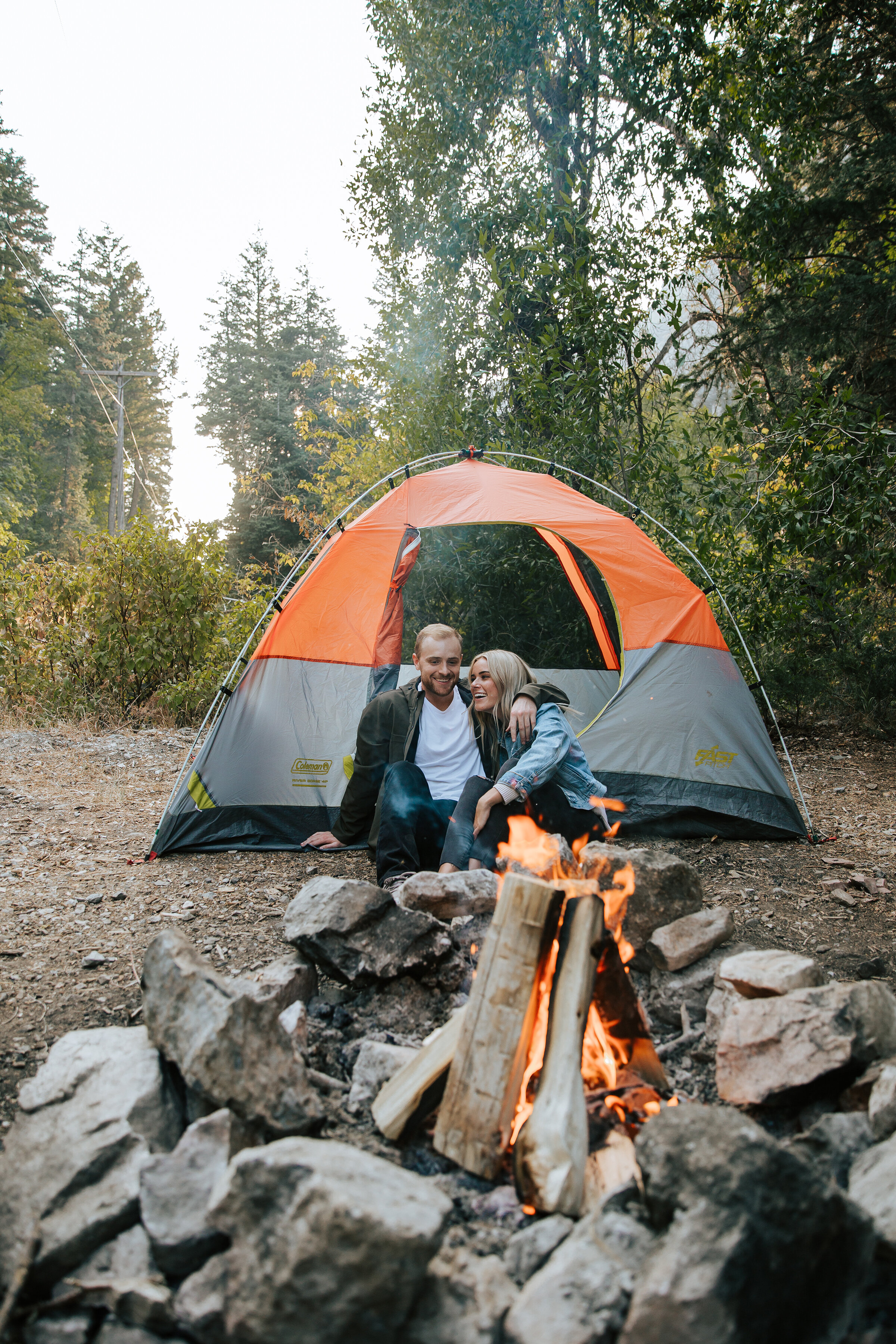  A happy couple sit in front of the fire in a camping styled engagement photo shoot in Utah. Engagement photo shoot location inspiration photo shoot aesthetic inspiration camping woodsy outdoors engagement goals couple goals camping goals couple sitt