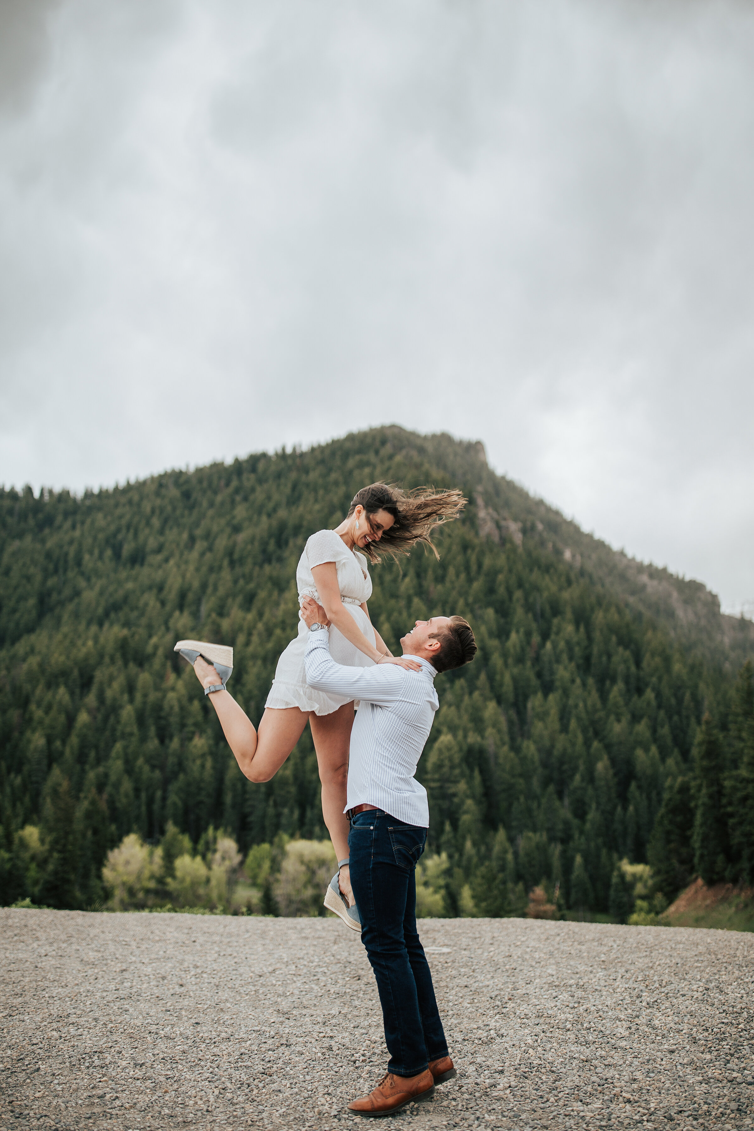  A playful man lifts his fiancé up in a beautiful mountain area in Utah in an engagement session by professional Utah photographer Emily Jenkins Photography. Couple pose inspiration ideas and goals outdoor photo shoot inspiration ideas and goals Utah