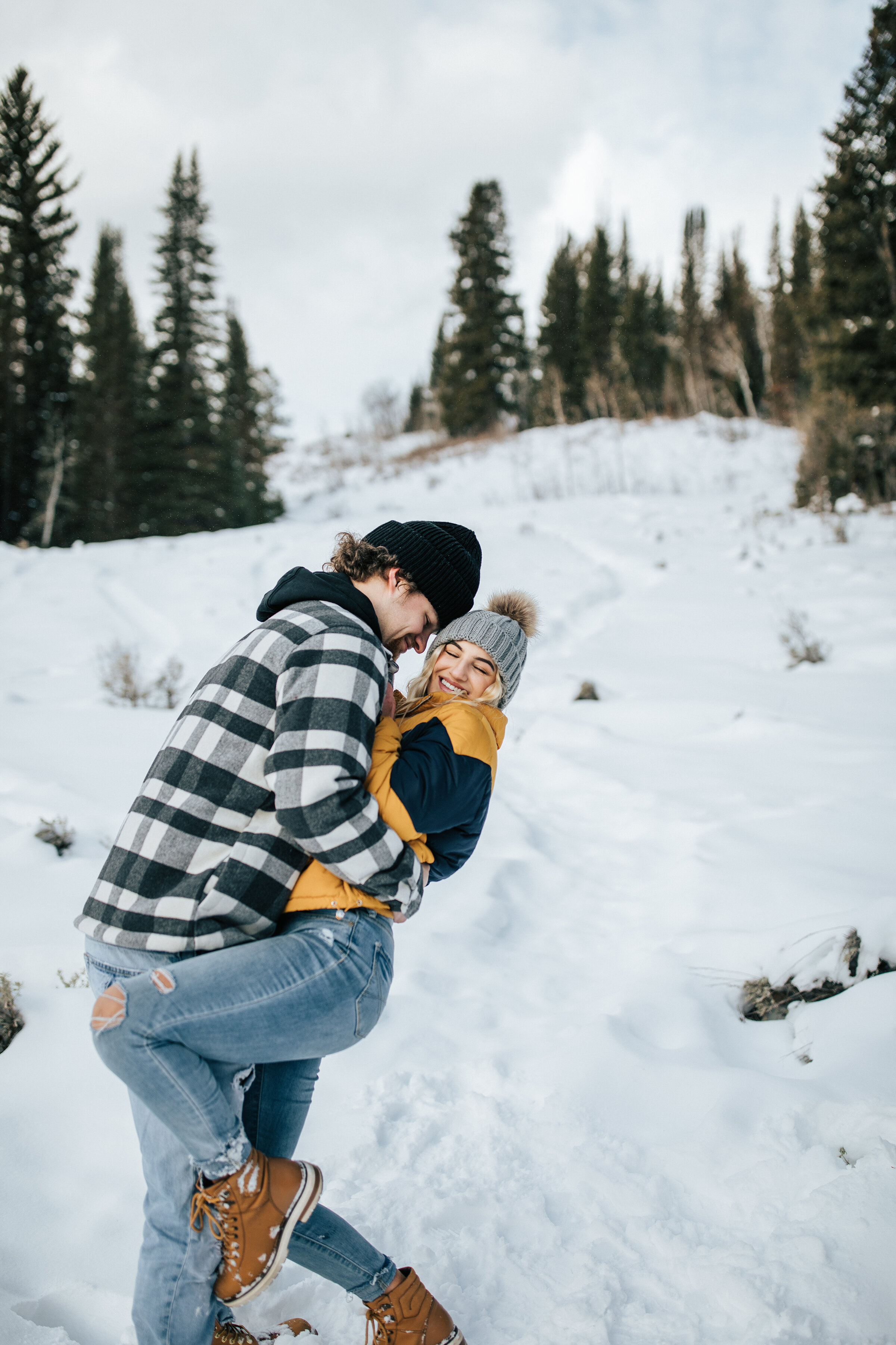  A happy couple play in the snow in a beautiful snowy engagement shoot in Utah by Emily Jenkins Photography. Winter photo shoot attire inspiration ideas and goals client attire for winter photo shoot in the snow professional Utah photographer playful