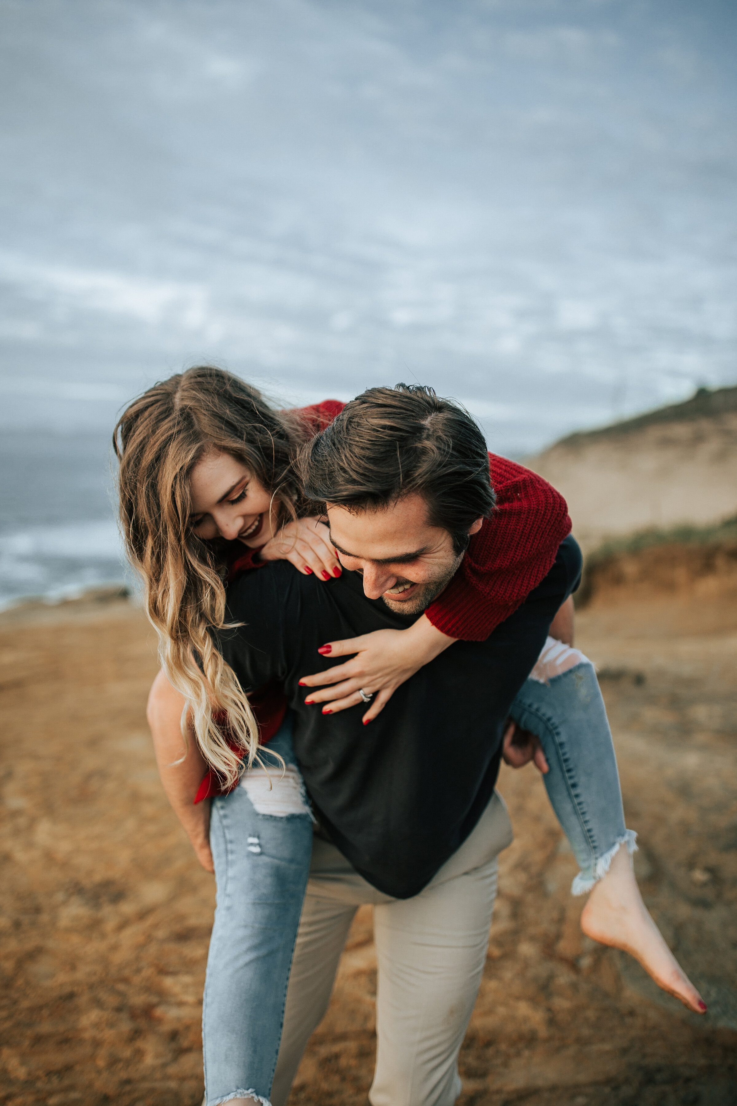  A newly engaged couple play on the sand dunes in a playful engagement session by Emily Jenkins Photography. Playful couple pose inspiration couple goals outdoor engagement session inspiration ideas and goals cloudy day engagement session inspiration