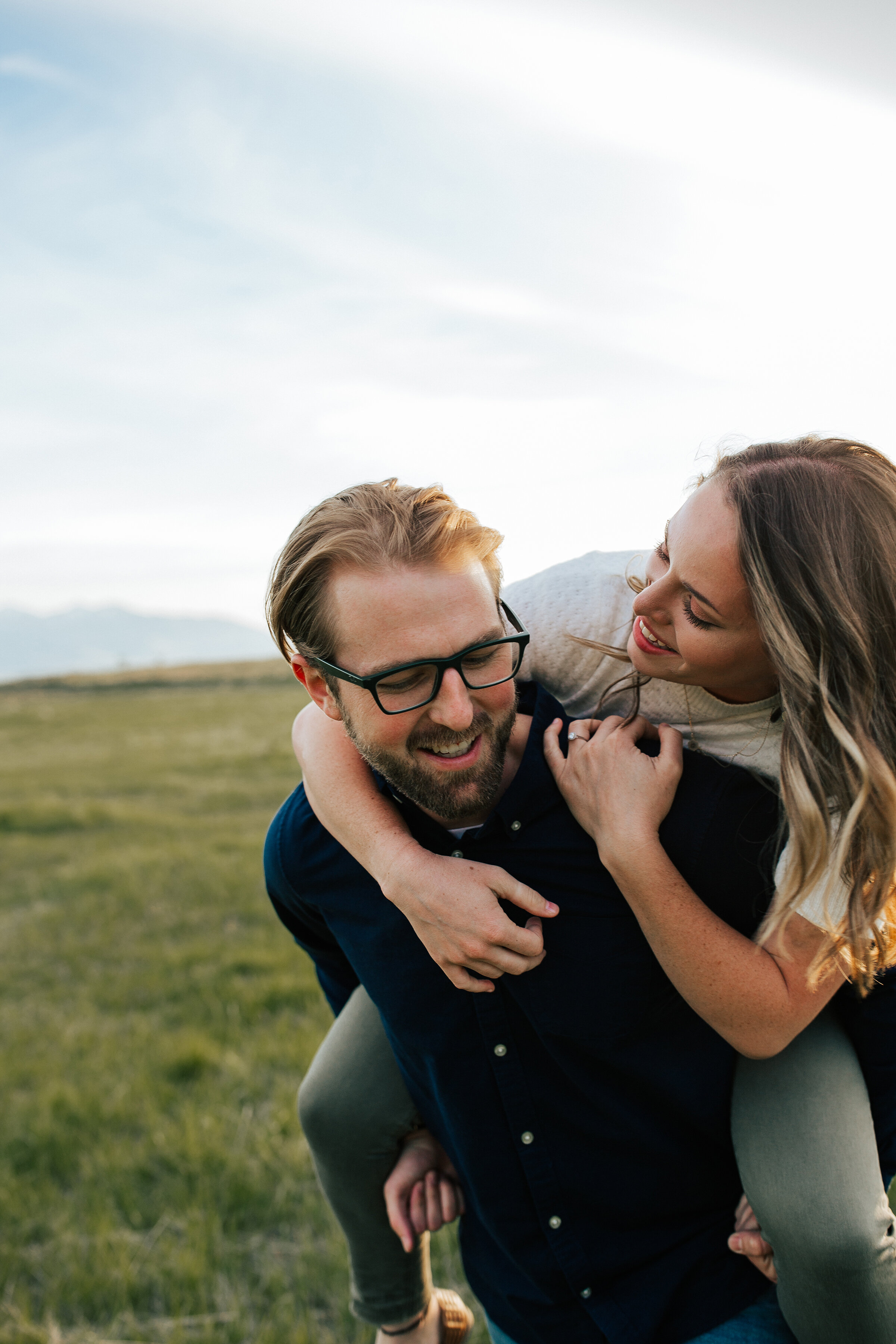  A man gives his fiancé a piggy back ride in a playful engagement session in the summer. Emily Jenkins Photography professional Utah photography playful couple pose inspiration ideas and goals couple goals outdoor engagement session inspiration ideas