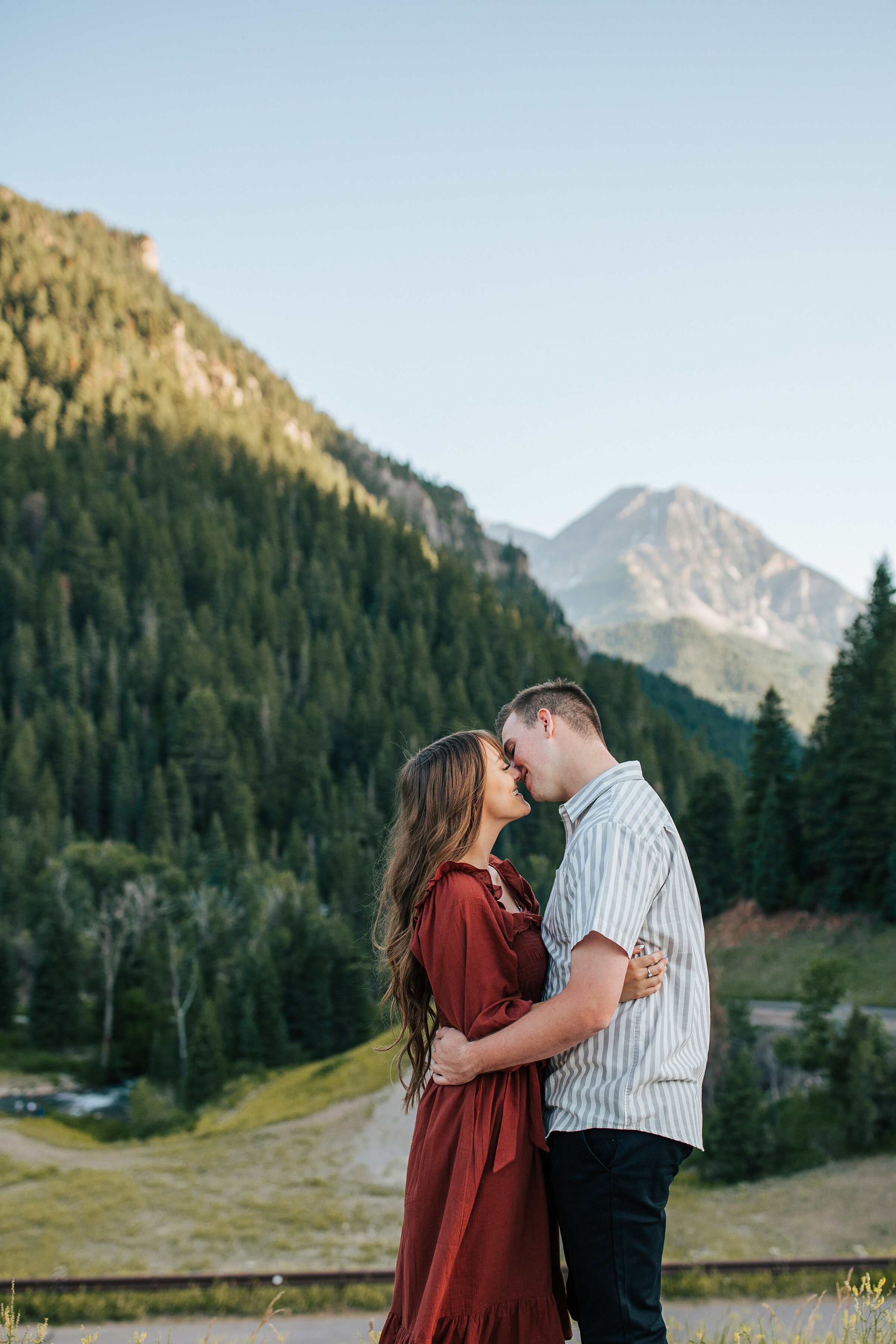  A beautiful couple kiss in the tree covered mountains in a beautiful summer engagement session by professional photographer Emily Jenkins Photography. Client attire inspiration for engagement sessions summer engagement session couple goals couple po
