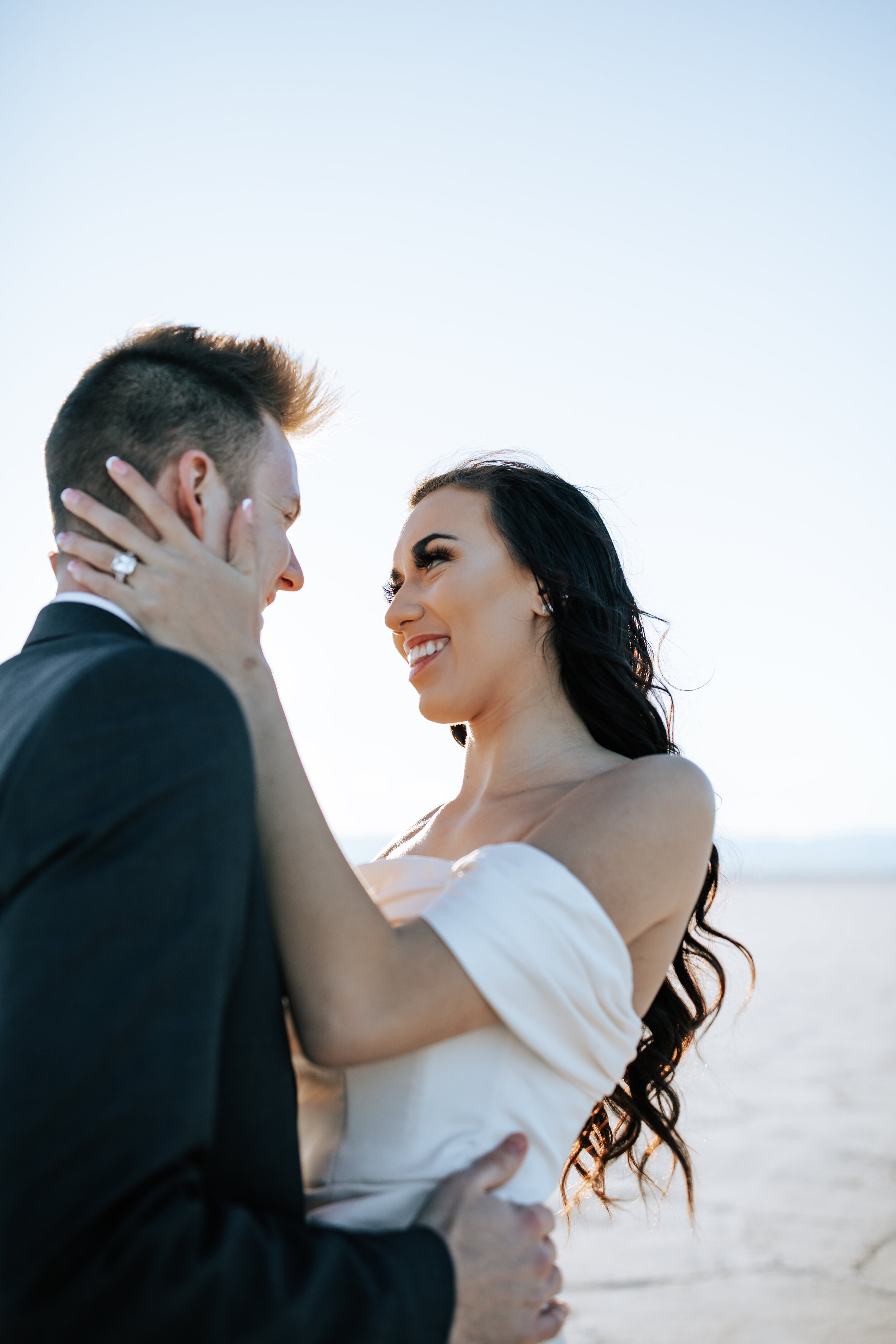  Couple on the Utah Salt Flats with women holding man's face smiling at him captured by Emily Jenkins Photography. Man and wife vow renewal photo couple goals vow renewal style vow poses vow renewal photography wedding redo celebrate anniversary salt