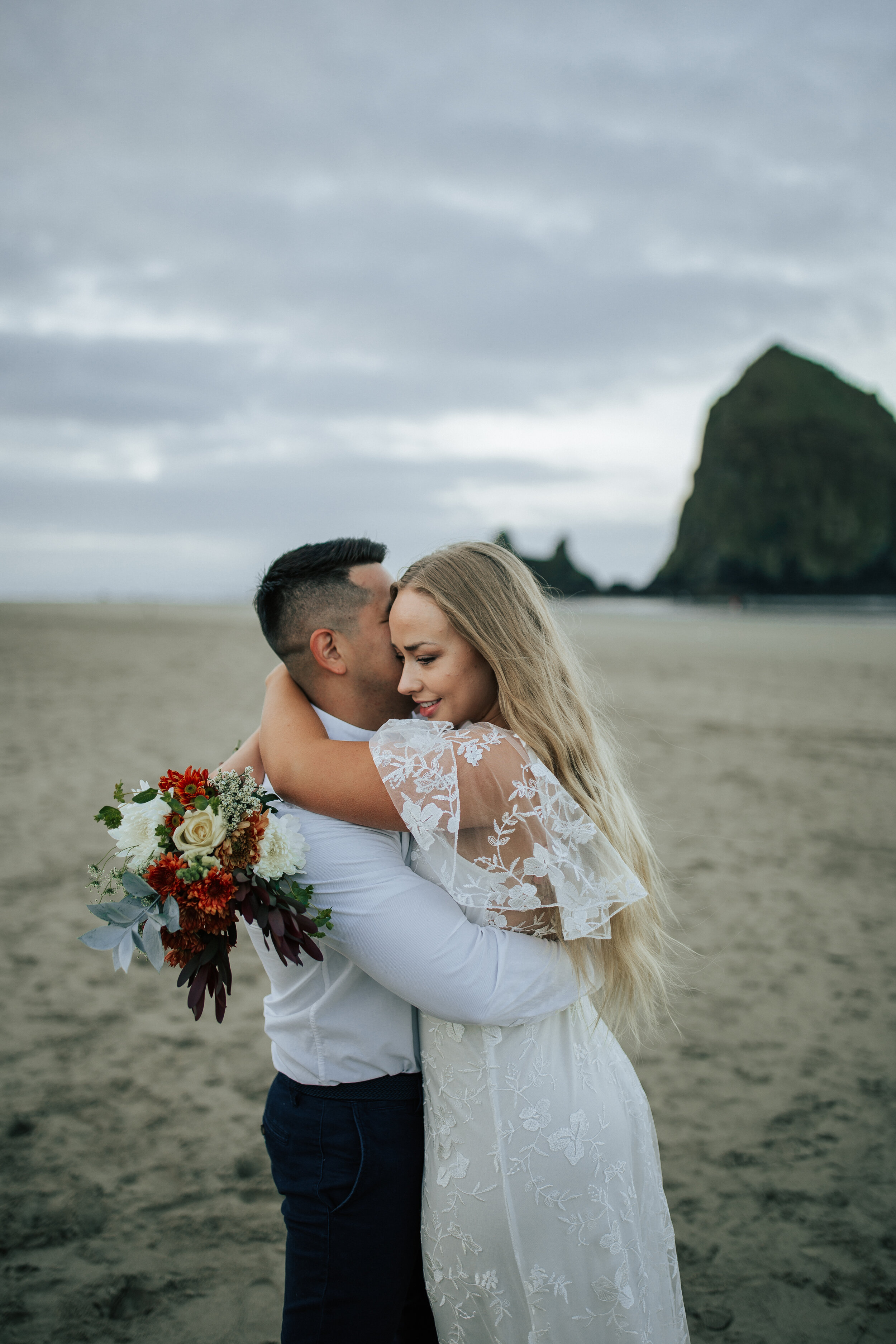  Husband and wife holding each other on Oregon coast beach landscape during vow renewal by Emily Jenkins Photography. Vow renewal poses vow travel ideas vow renewal dress lace dress beach renewal couple photography Oregon coast travel photography lin