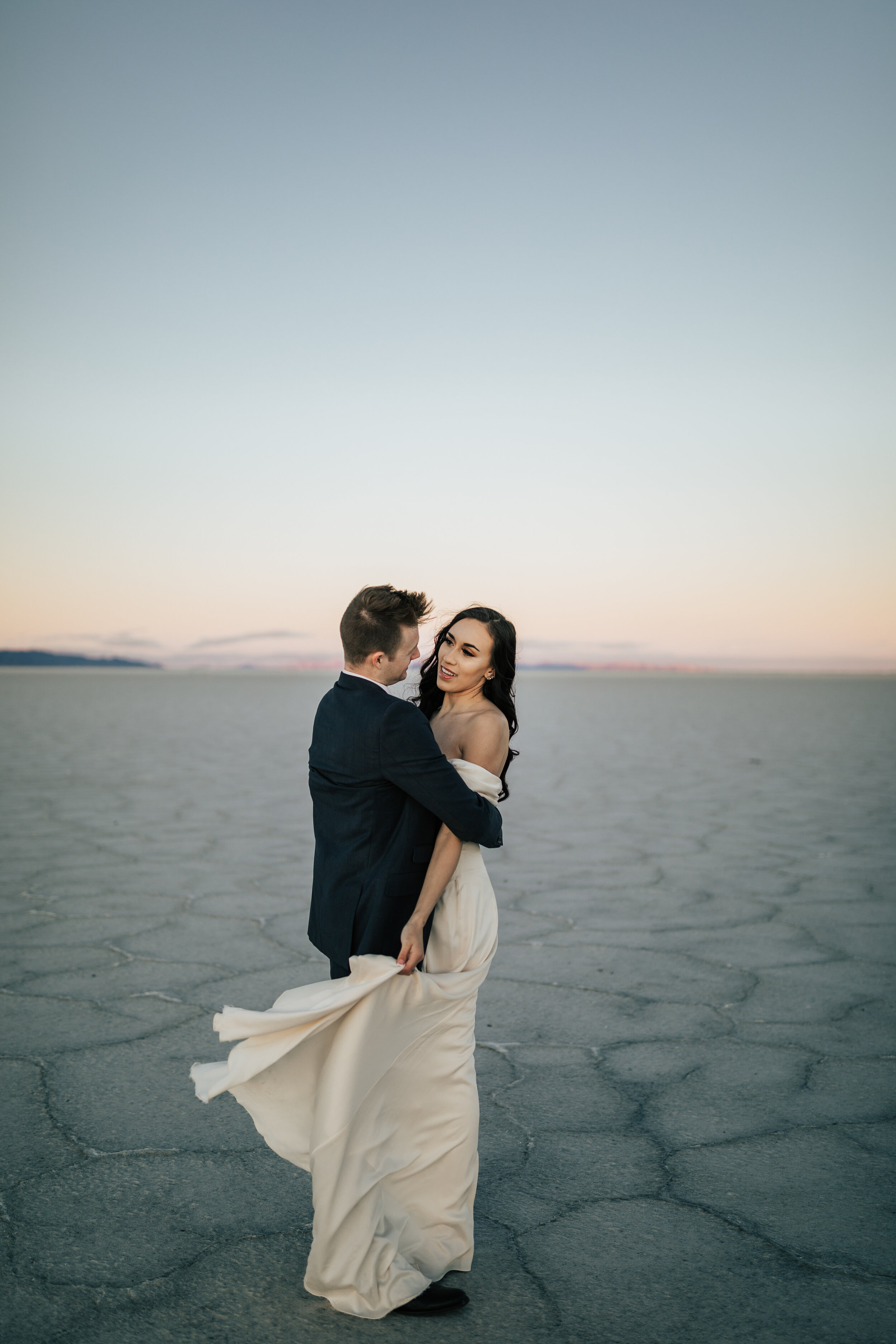  Emily Jenkins Photography photo of a man holding a woman in a beautiful off-the-shoulder cream vow renewal dress in the middle of the Salt Flats in Utah. Wedding redo celebrate anniversary couple photographer Park City photography off the shoulder d