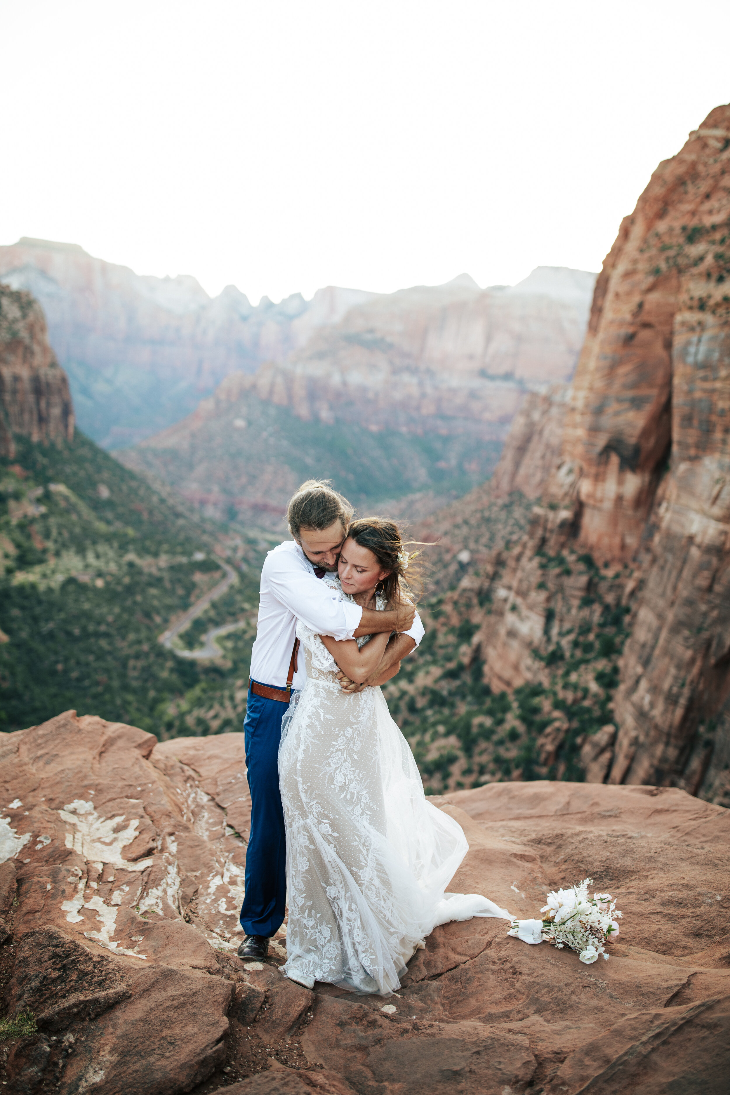  A handsome groom hugs his beautiful bride on the rocks of Zion National Park, Utah in a stunning elopement styled photo shoot by professional wedding photographer Emily Jenkins Photography. Couple pose inspiration ideas and goals outdoor photo shoot