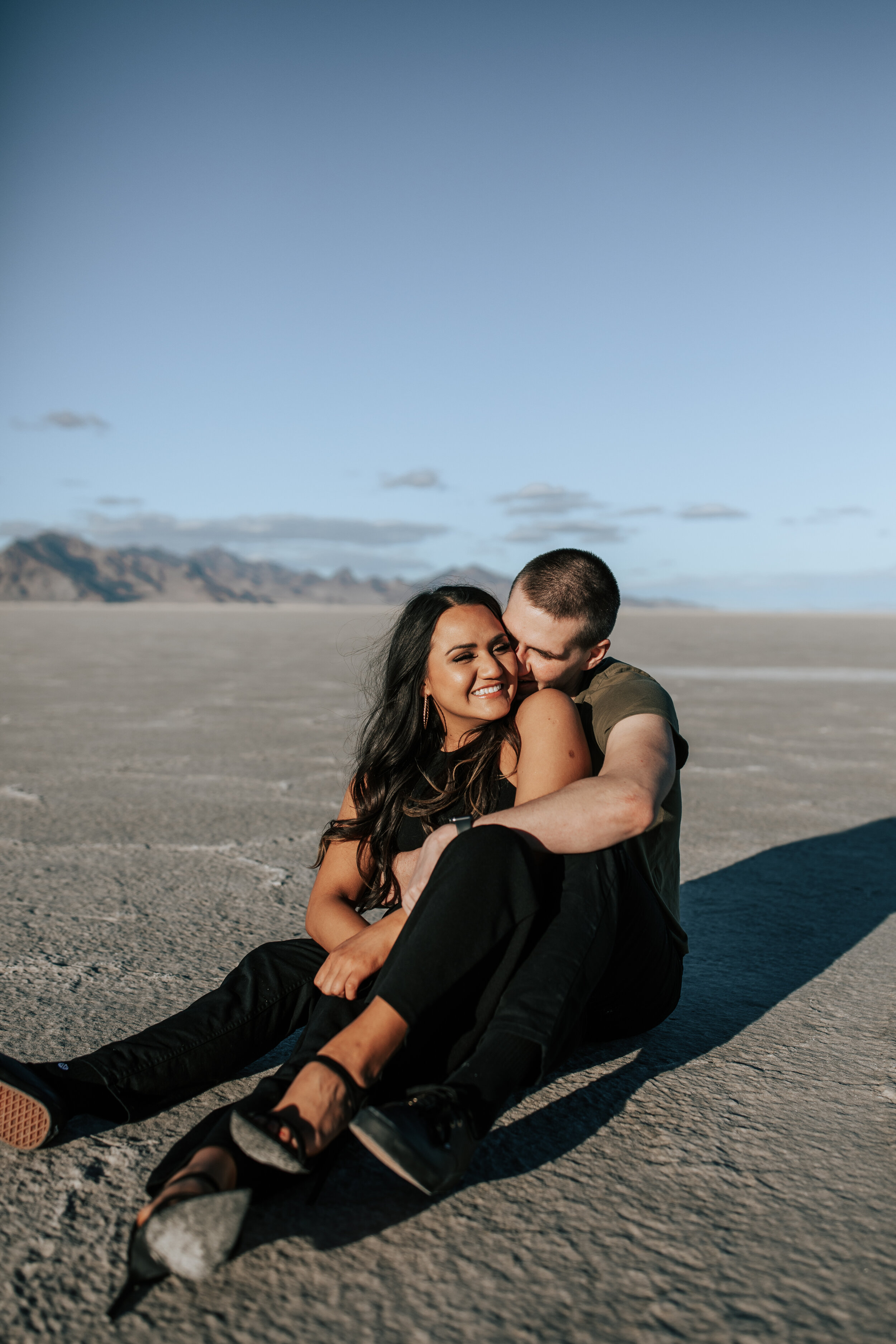  Emily Jenkins a SLC Photographer captures man straddling woman and kissing her cheek on the Salt Flats. Utah salt flats photo cute utah couples salt lake city photography black outfit ideas for pictures couple goals pure love sunrise #utahcouplephot