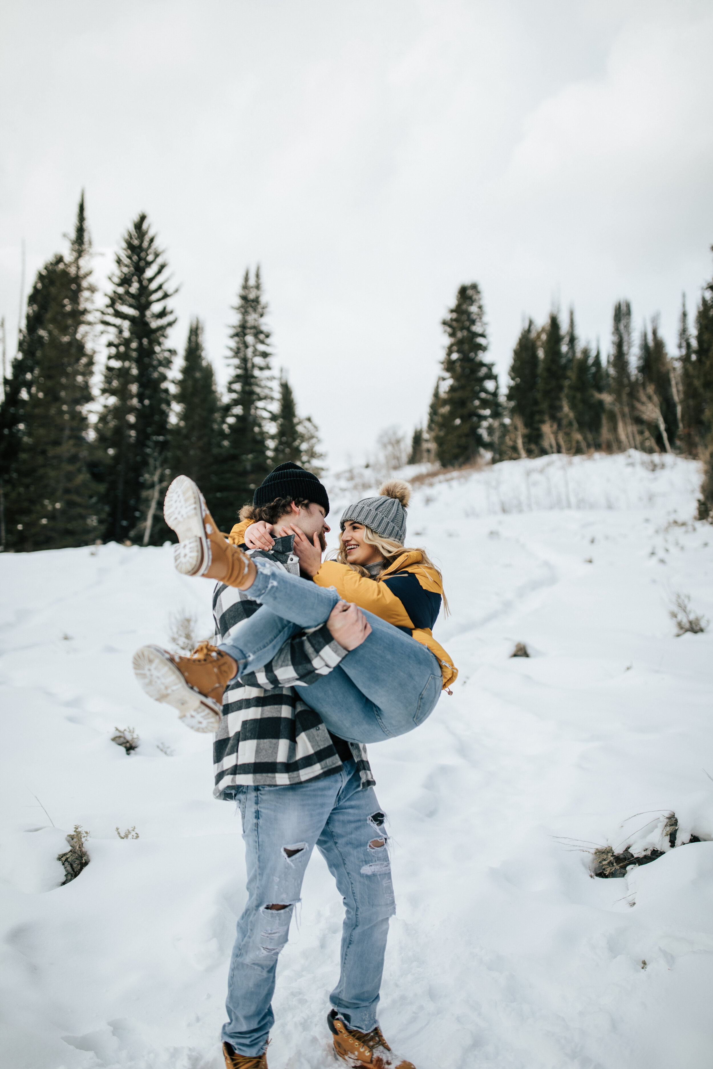  Man holding woman in a cradle pose during Salt Lake City, Utah winter with snow captured by Emily Jenkins Photography. Park city couple photo snow pictures salt lake city photographer utah winer photography couple in beanies utah snow vacation winte