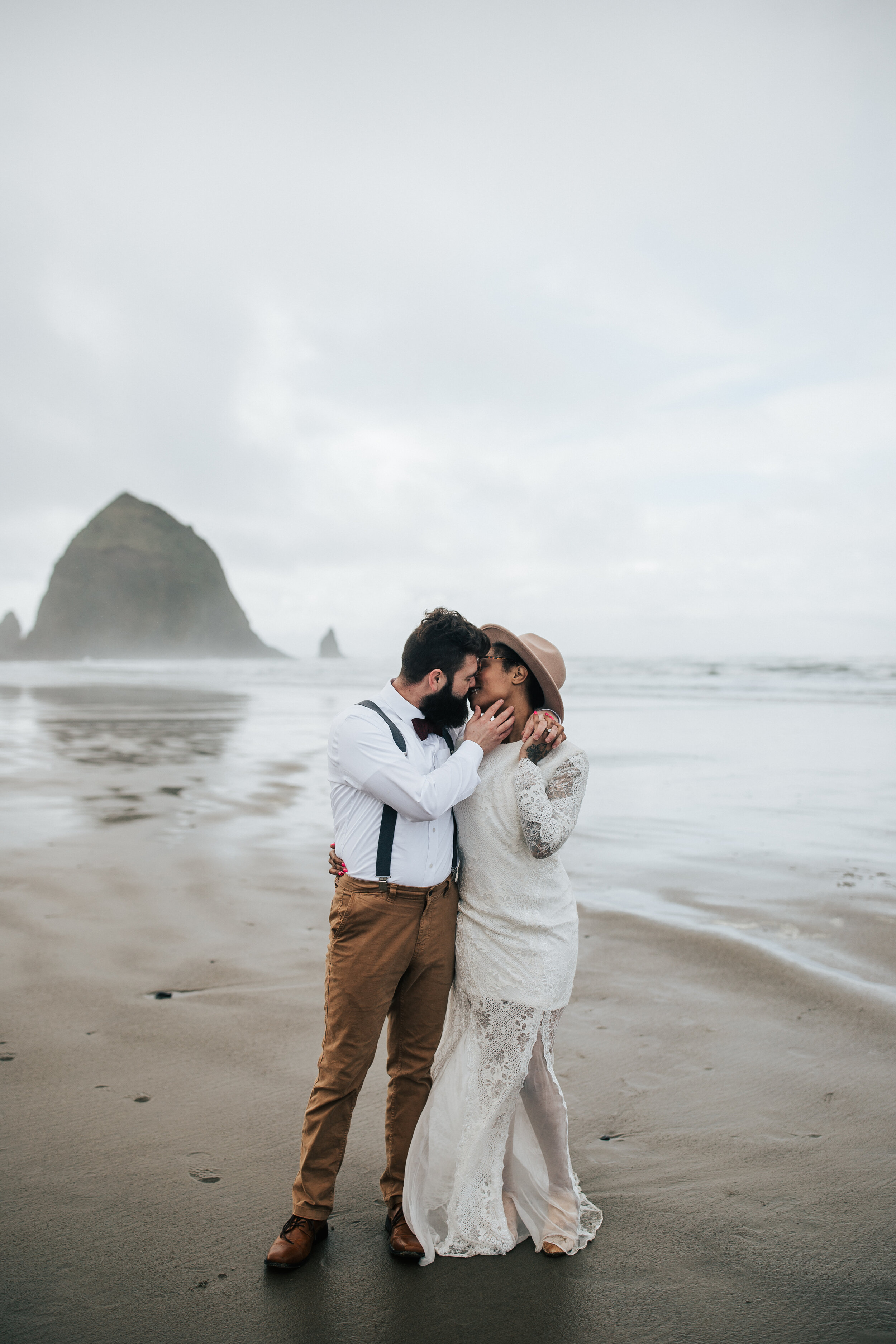   Eloping on the Oregon coast with keyhole back wedding dress. Man and woman hold hands at Cannon Beach, Oregon walk along the beach Oregon coast elopement photographer for adventurous couple #EmilyJenkinsPhotography #cannonbeach #elopementphotograph
