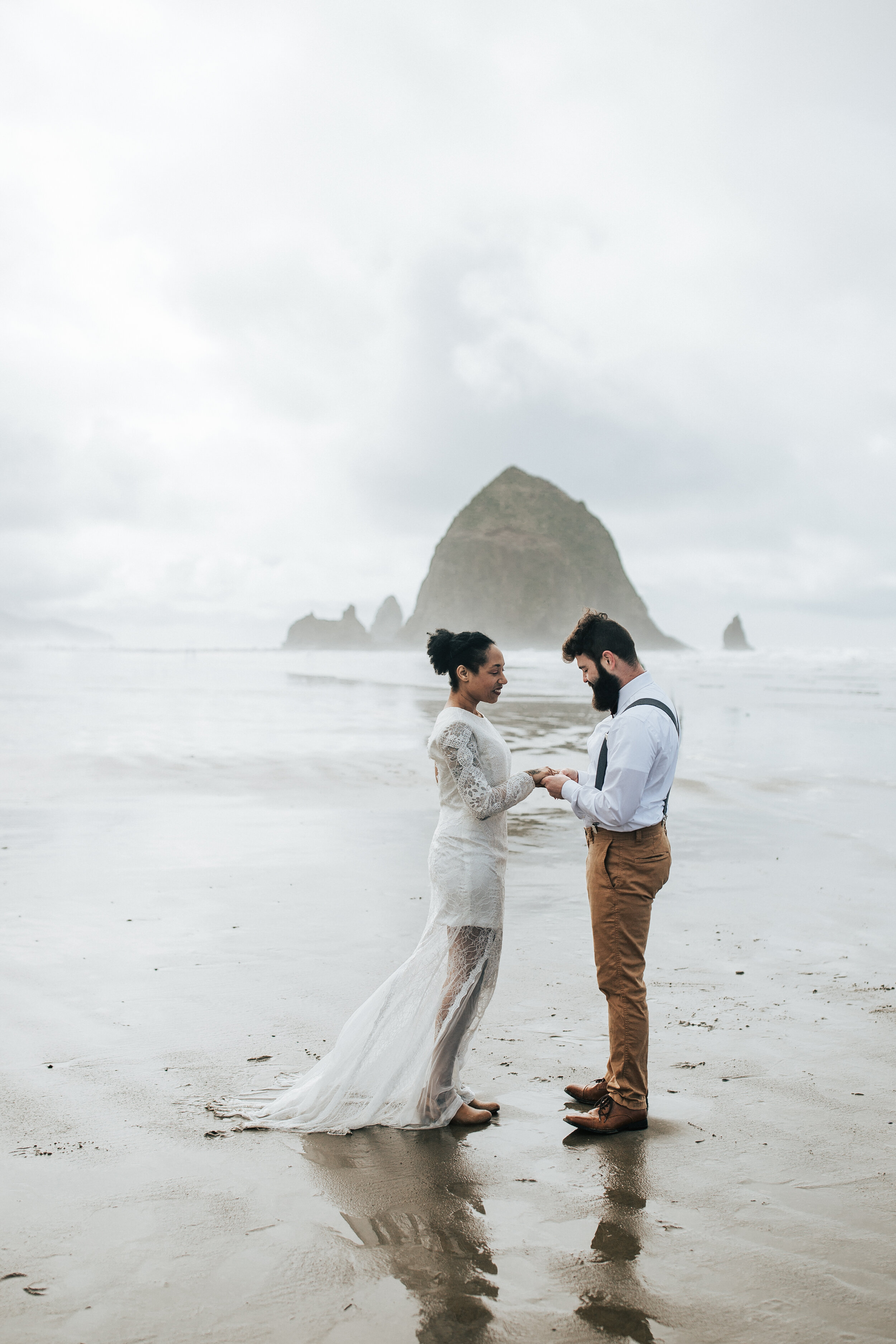  Eloping on the Oregon coast with keyhole back wedding dress. Man and woman hold hands at Cannon Beach, Oregon walk along the beach Oregon coast elopement photographer for adventurous couple #EmilyJenkinsPhotography #cannonbeach #elopementphotographe