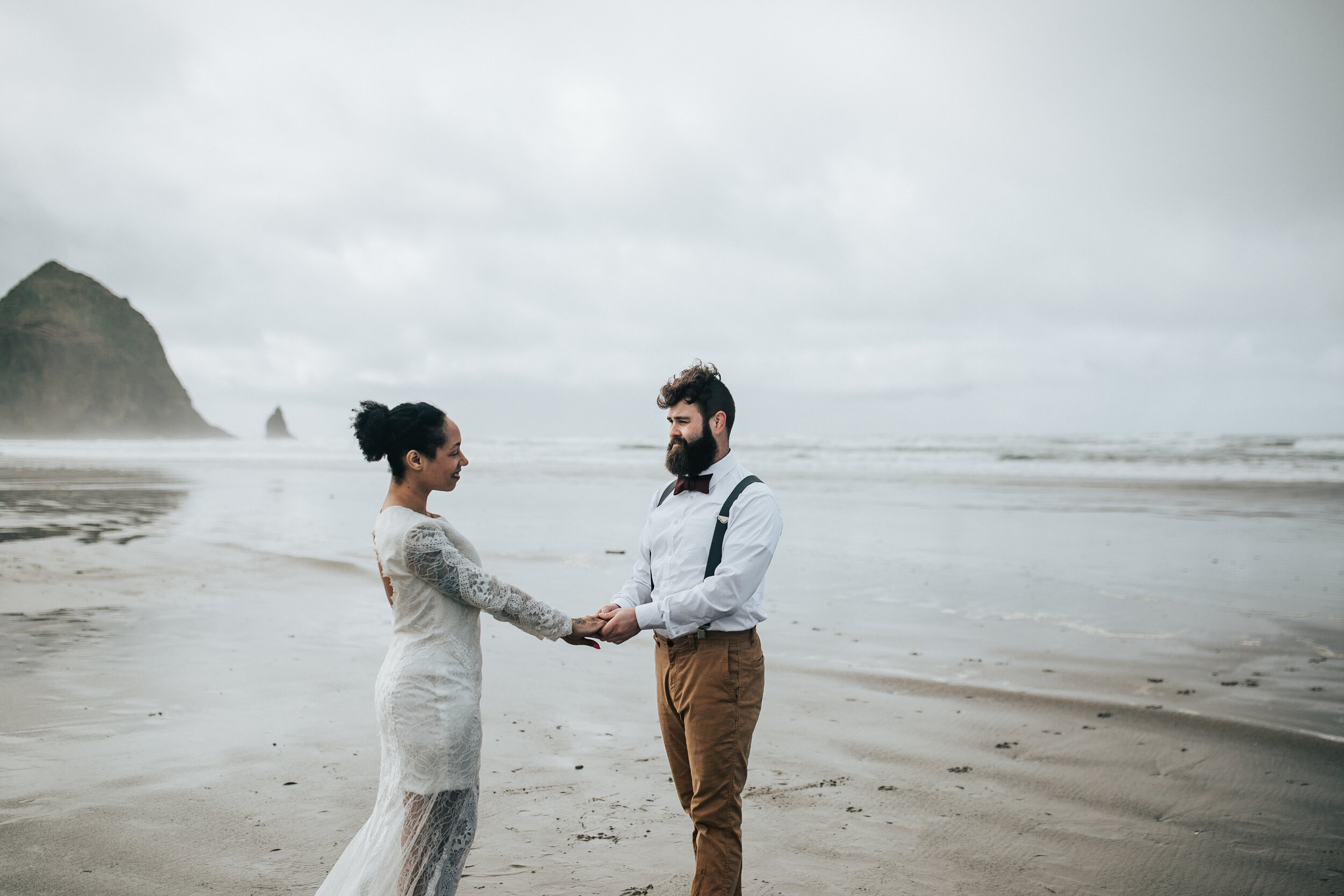  Eloping on the Oregon coast with keyhole back wedding dress. Man and woman say vows to each other at Cannon Beach, Oregon walk along the beach Oregon coast elopement photographer for adventurous couple #EmilyJenkinsPhotography #cannonbeach #elopemen