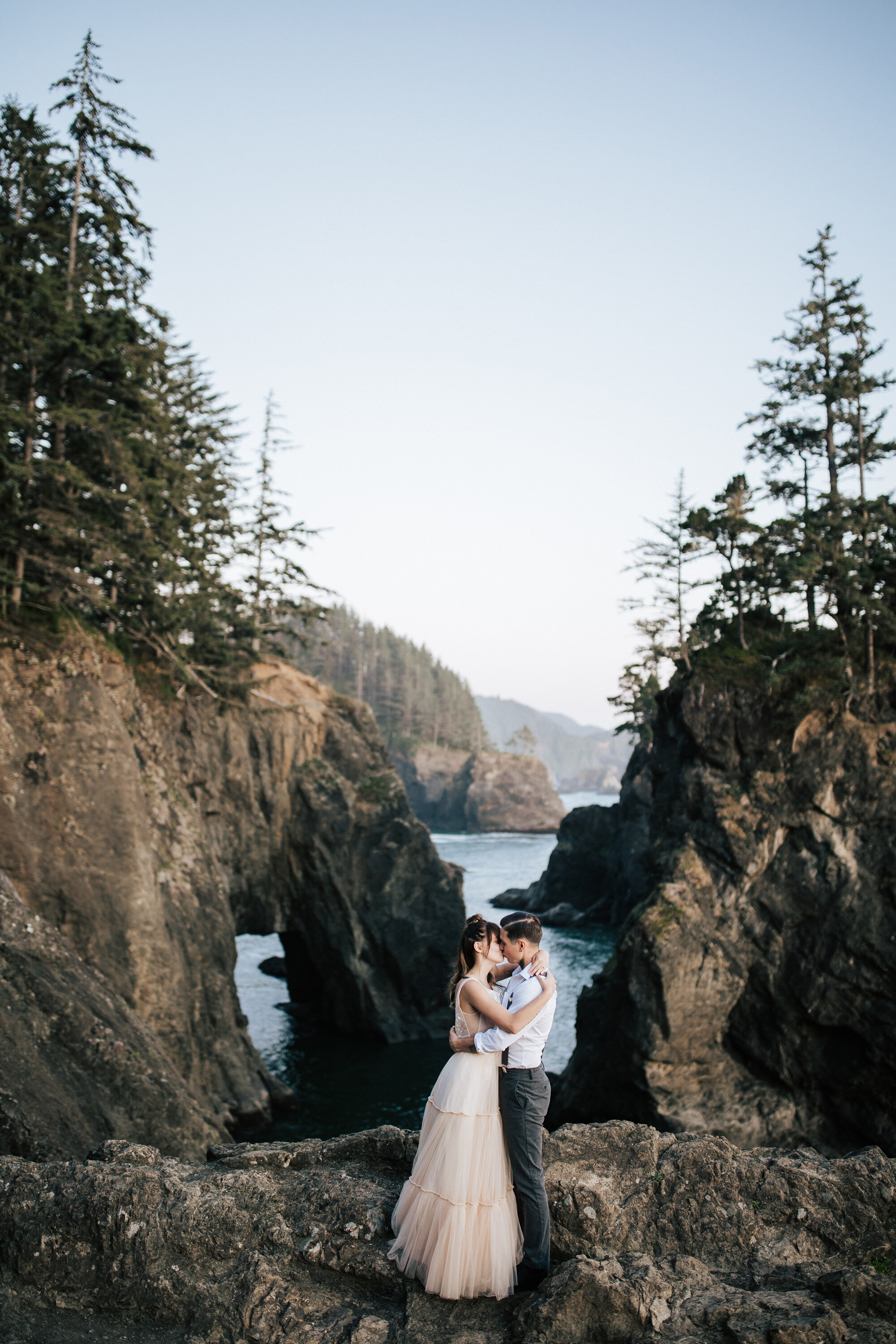  Newly married couple kisses during an elopement session with Emily Jenkins Photography in Brookings, Oregon featuring a blush pink wedding gown and cliff ocean overlook. cliff ocean overlook wedding elopement dress ideas couple photography Oregon #e