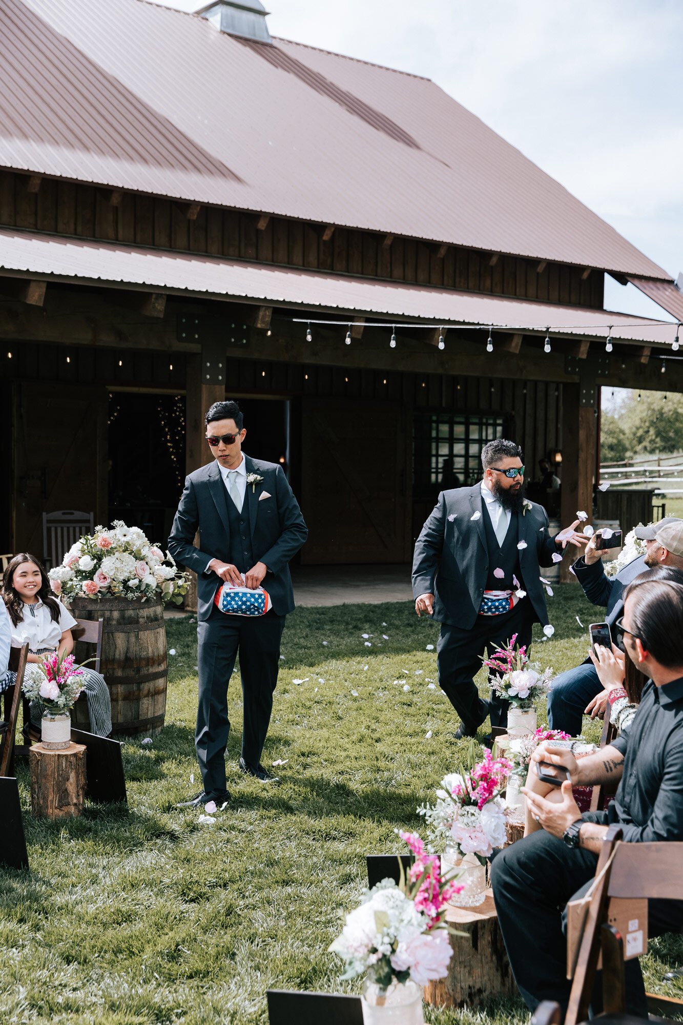  Flower boys walking down the aisle at Quiet Meadow Farms with American fanny packs throwing petals from them by Emily Jenkins Photography. flower guys with fanny packs creative flower girl replacements farm wedding venue #emilyjenkinsphotography #em