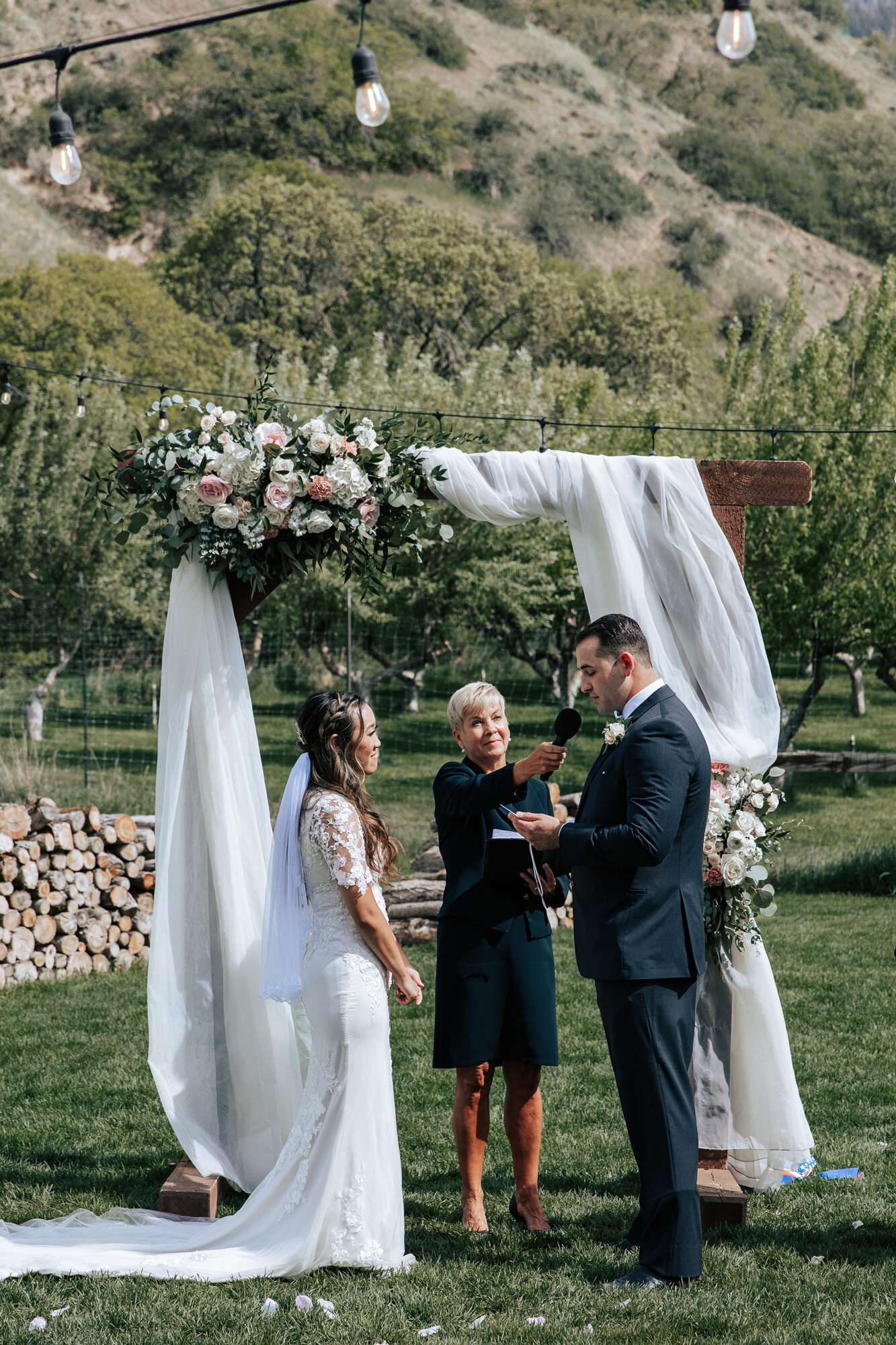  Pastor holds the microphone for the groom as he reads his vows with a white tulle altar with roses on it at Quiet Meadow Farms by Emily Jenkins Photography. groom reads vows Utah summer wedding flower petals #emilyjenkinsphotography #emilyjenkinswed