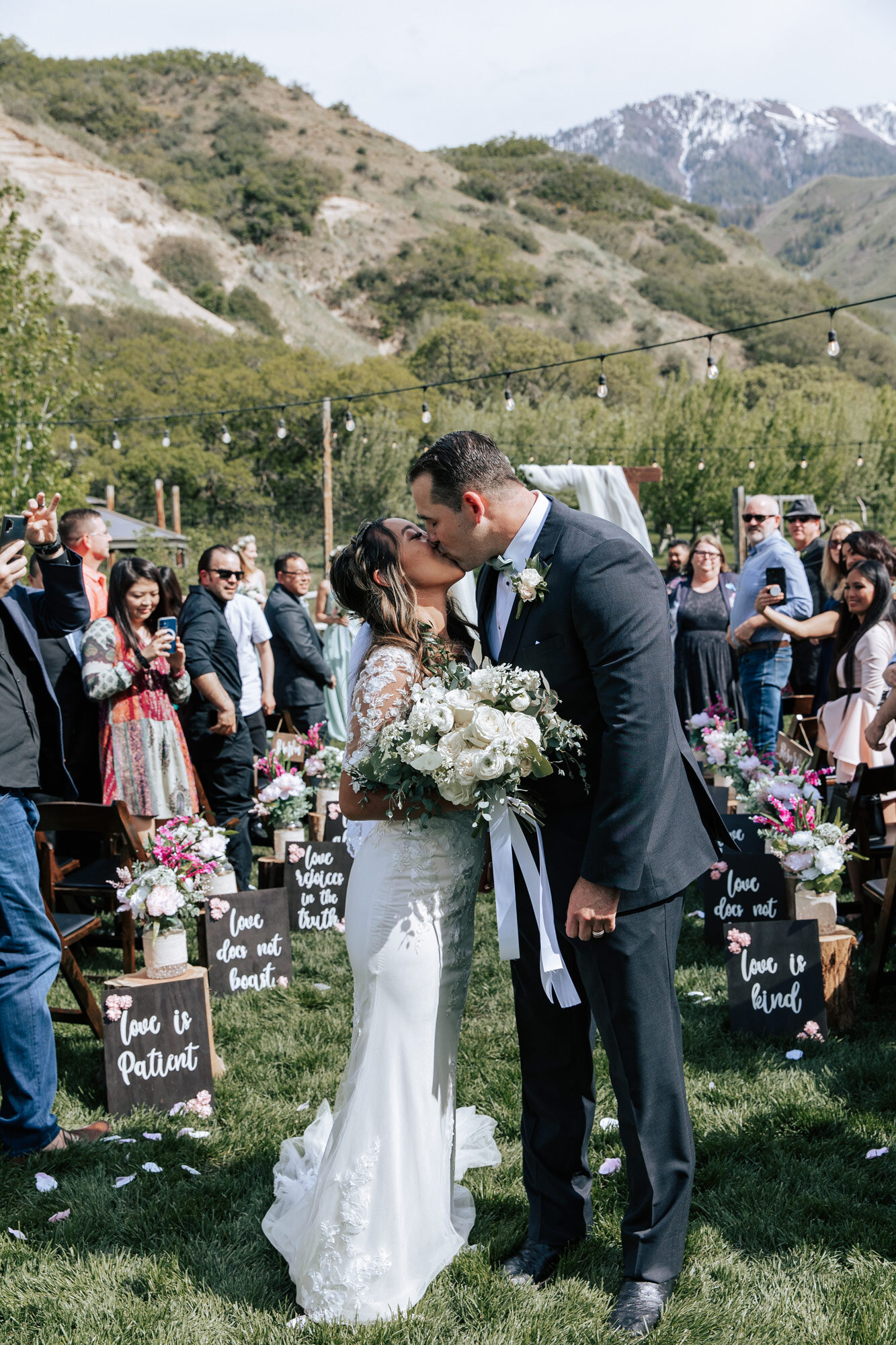  Bride holding a beautiful white summer bouquet kisses her husband in the aisle in between all of their wedding guests by Emily Jenkins Photography in Northern Utah. summer wedding wedding guest photo idea #emilyjenkinsphotography #emilyjenkinsweddin
