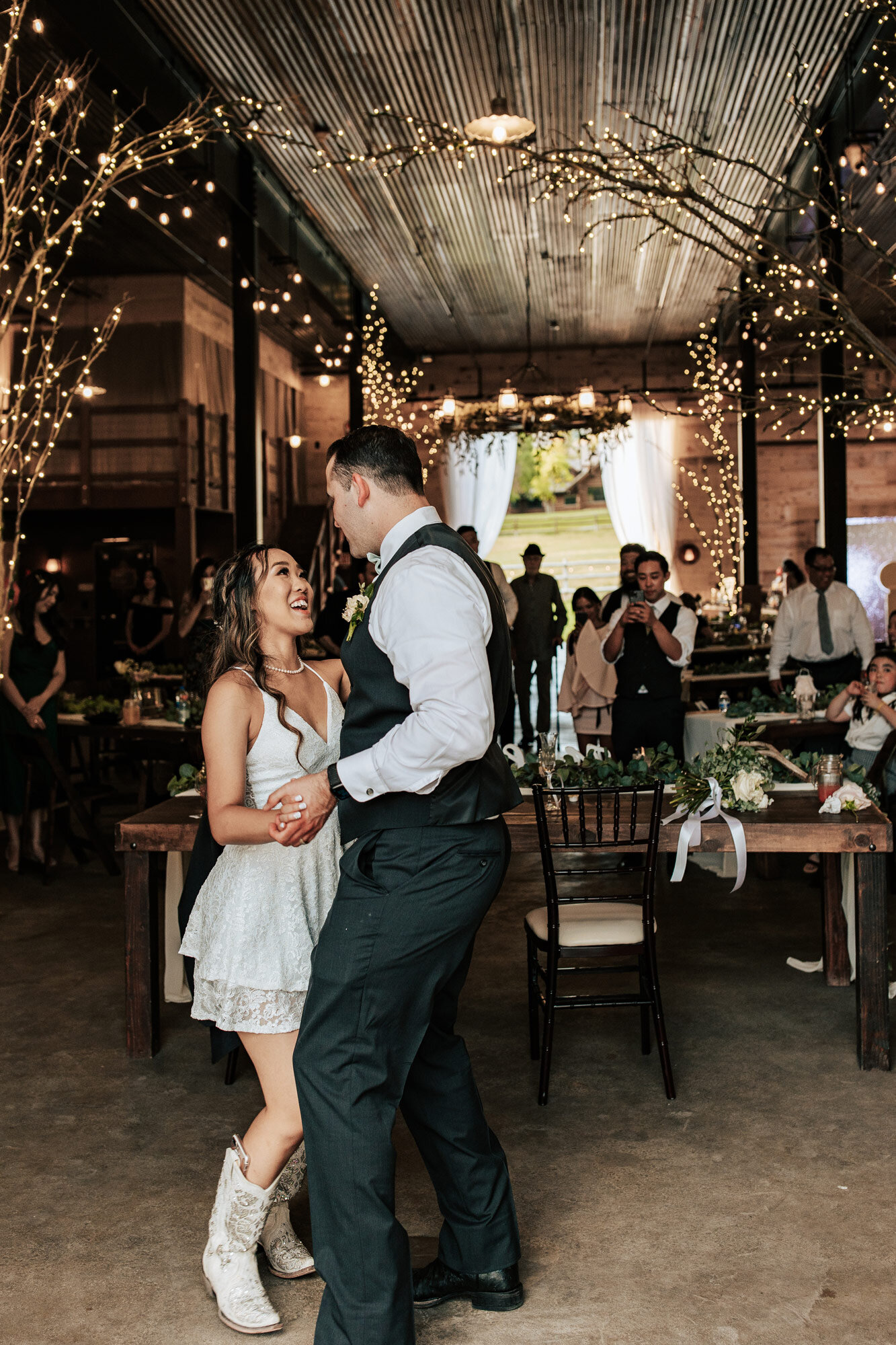  Emily Jenkins Photography captures a couple during their first dance with fairy lights about them and the bride in white cowgirl boots at Quiet Meadow Farms in Utah County. couples first dance short reception dress #emilyjenkinsphotography #emilyjen