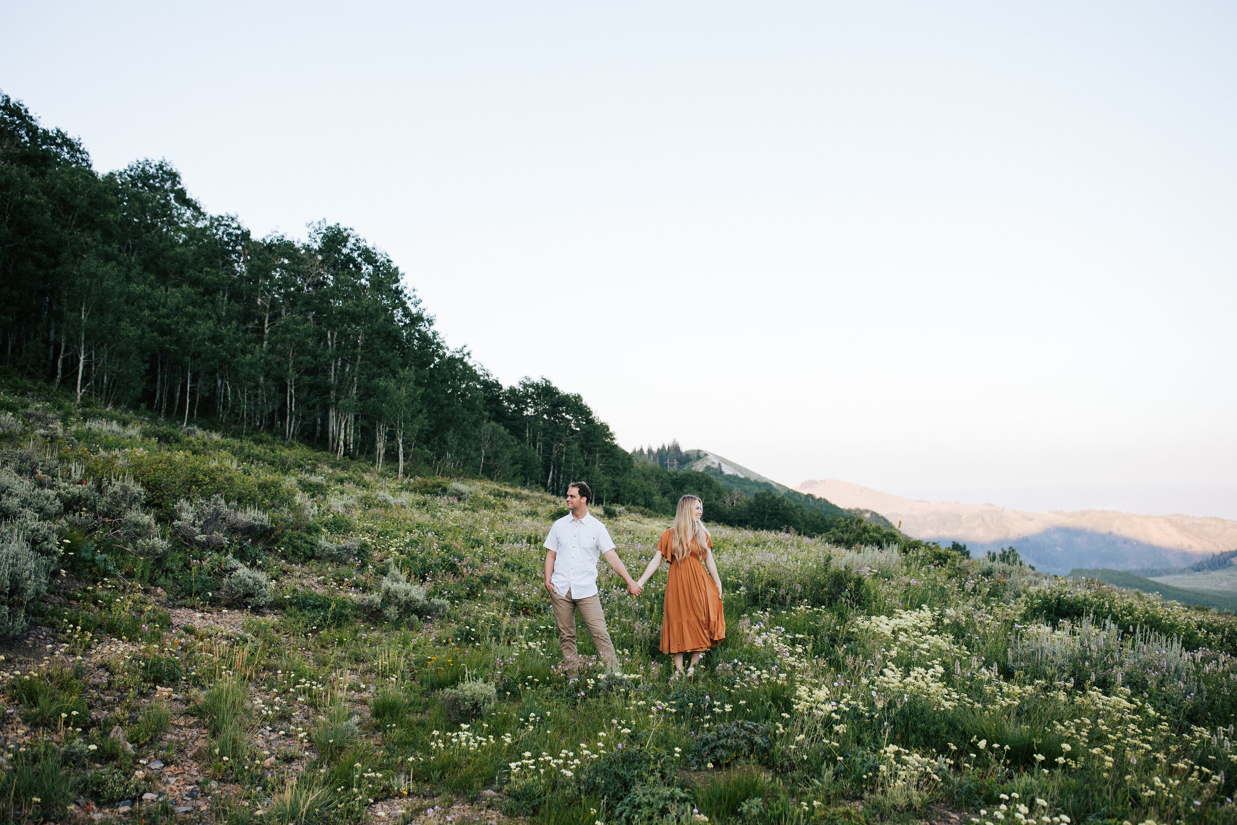  Engagement session in wildflowers in the mountains near Park City, Utah. Summertime engagement photos with mountain views. Engaged couple doing a piggyback ride in the mountains. Outfit inspo. Engagement outfits Wedding photographers in Utah county 