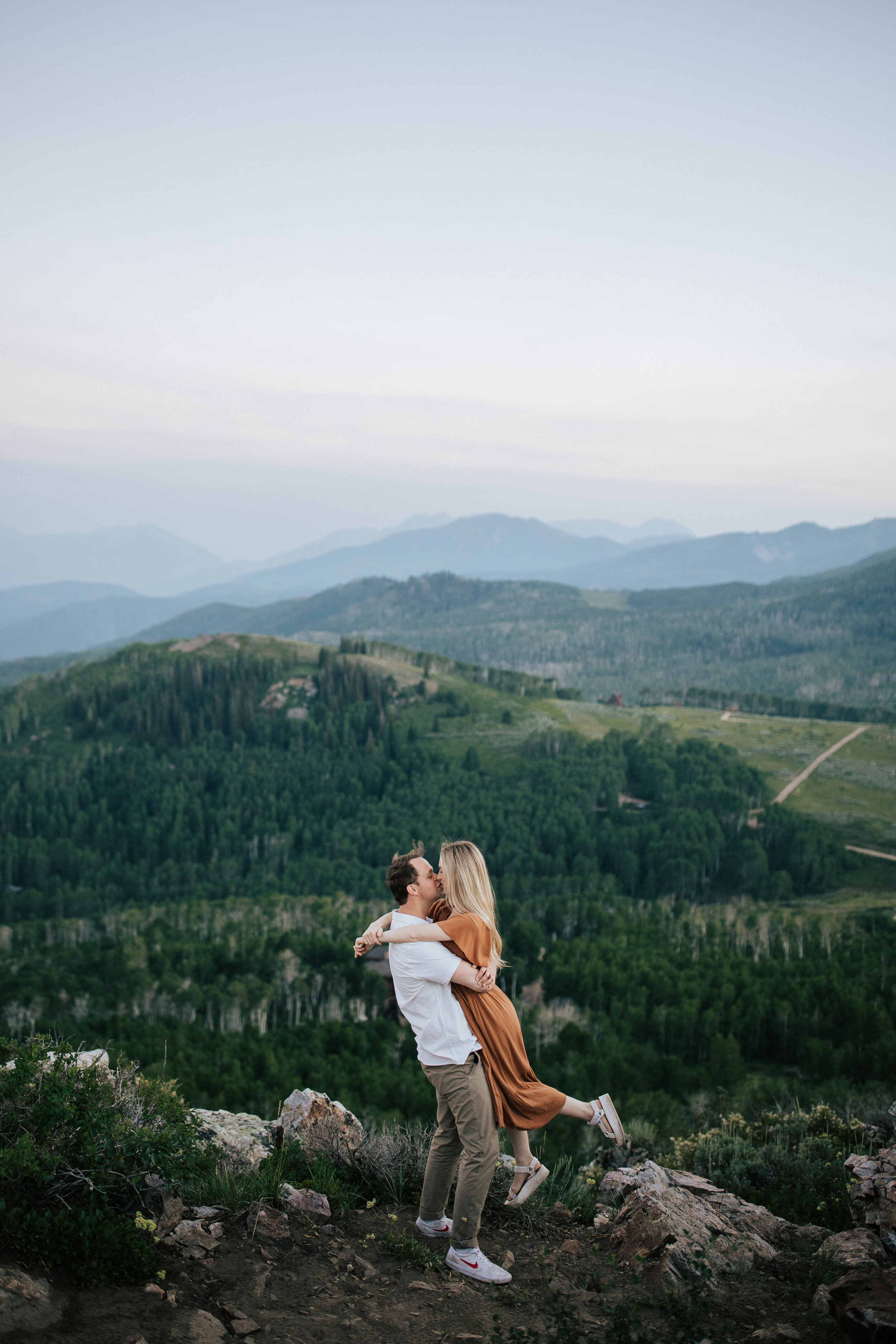  Engagement session in wildflowers in the mountains near Park City, Utah. Summertime engagement photos with mountain views. Engaged couple doing a piggyback ride in the mountains. Outfit inspo. Engagement outfits. Pine trees. #engagementphotos #engag