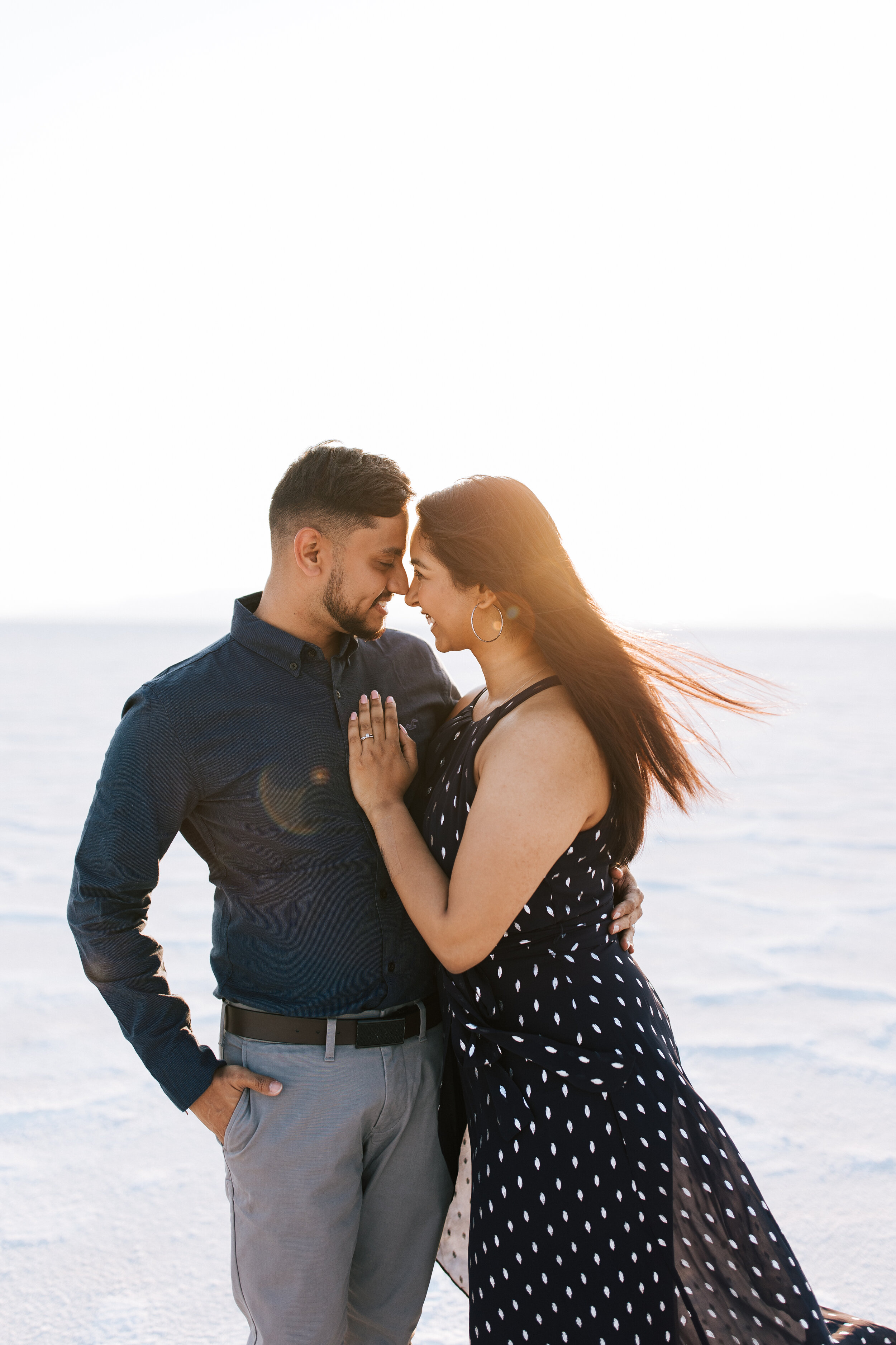  Couple walking at the Salt Flats Utah during their couples shoot with Emily Jenkins Photo. Golden hour lighting with flowy dress and nice outfits. #saltflats #photographer #engagements #couplesession 