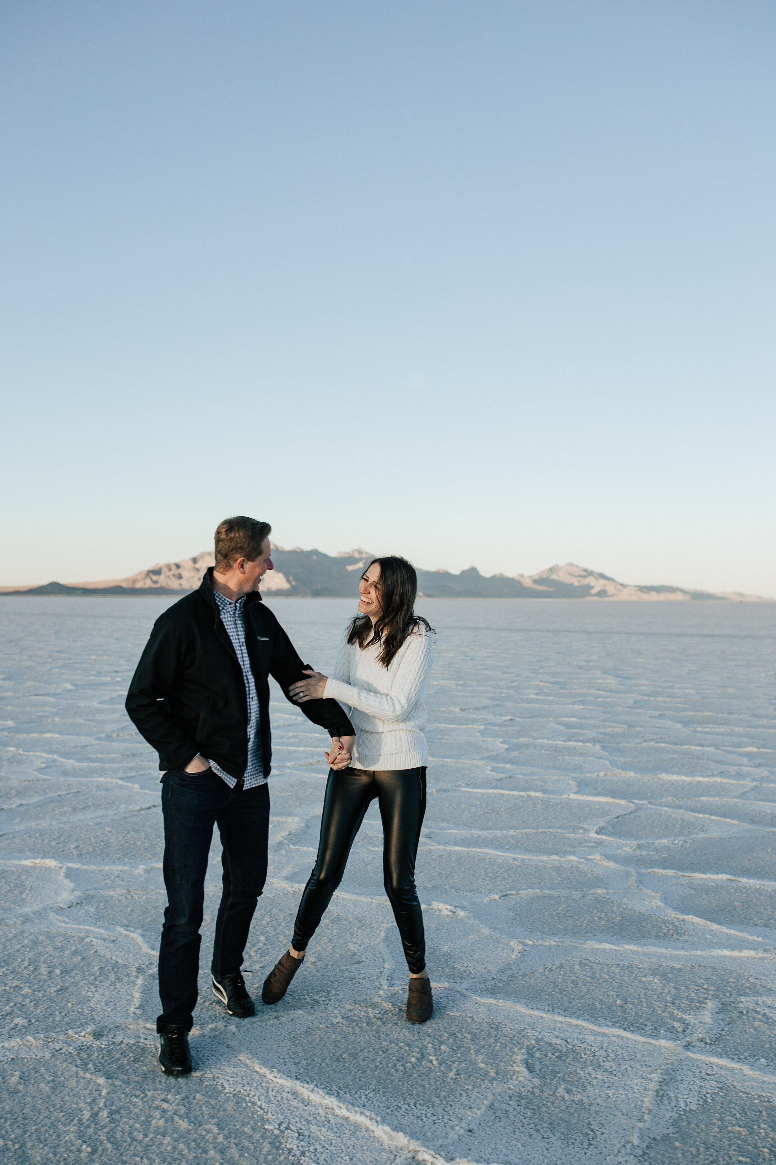  Bonneville Salt Flats couples session. Couple teases each other at the salt flats Utah. Winter couples shoot anniversary session in Utah. Adventurous couples shoot. #engagementsession #couplesession #coupleshoot #weddingphotography #elopement  