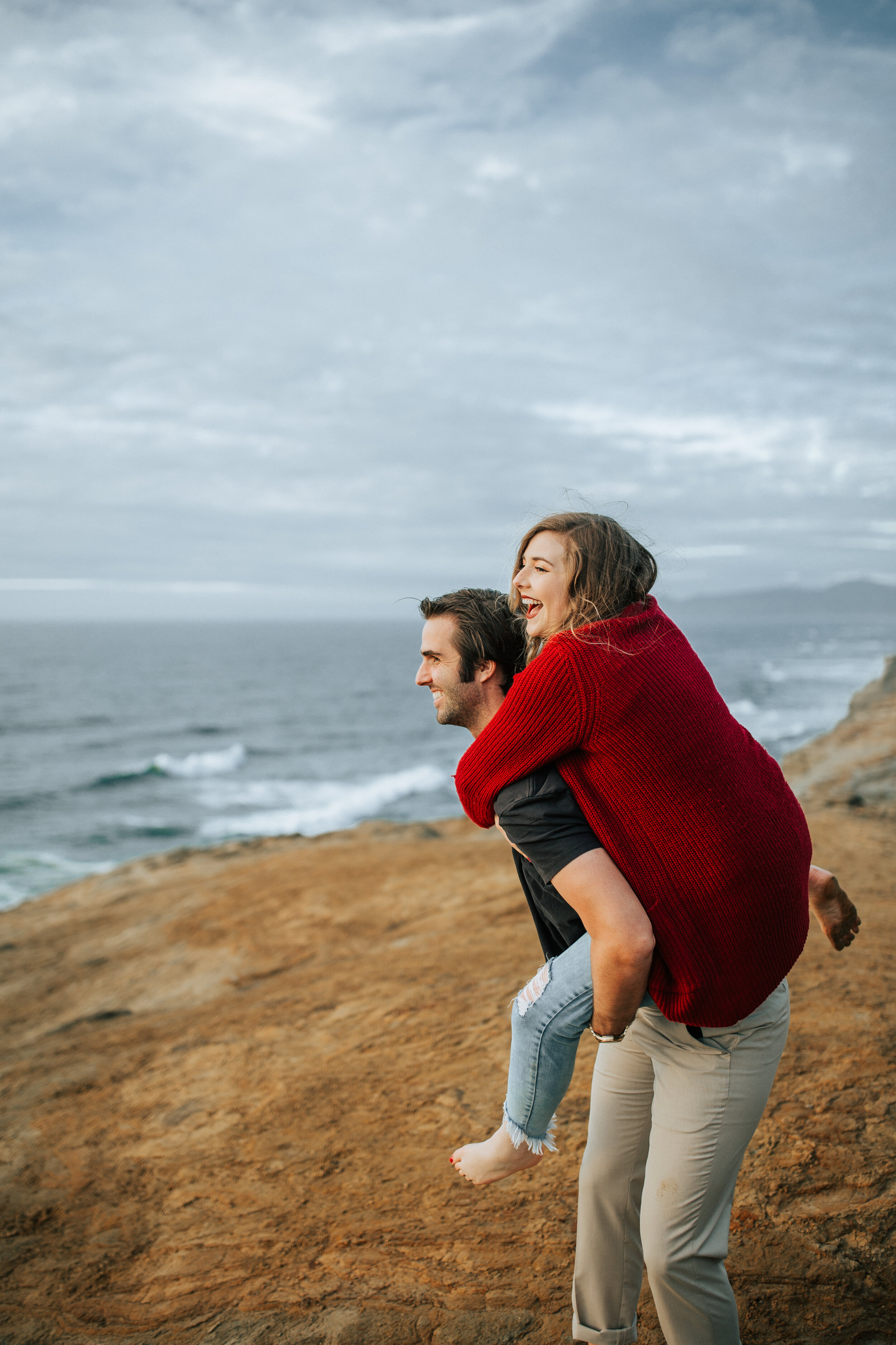  Couples session on the beach couple gives a piggyback ride on the Oregon coast. Pacific City Oregon engagement session. Couple laughing at Cape Kiwanda, Oregon. #oregonengagements #engagements #oregoncoast #photographer #weddingphotographer 