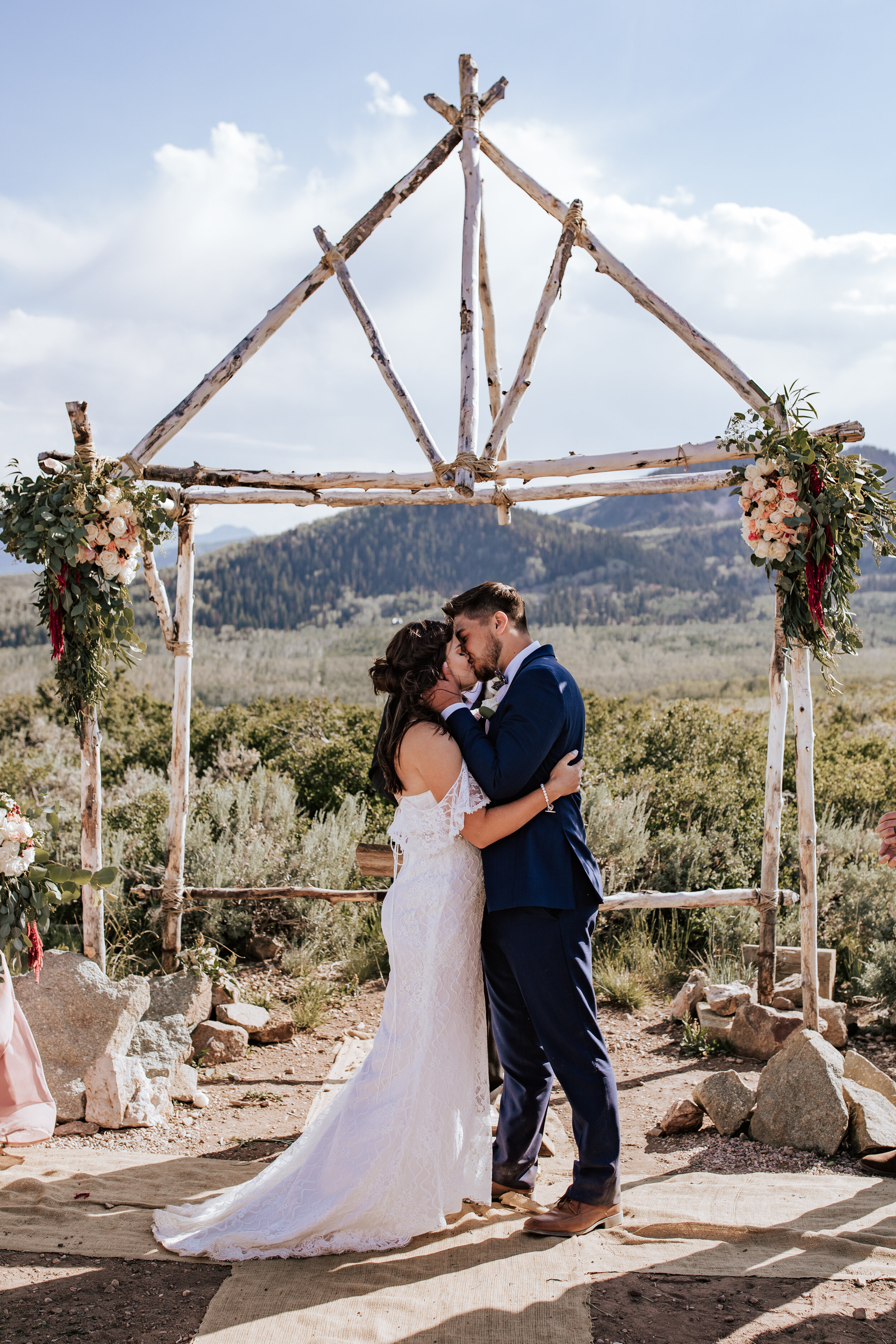  A couple kiss in front of a birch wood altar in the mountains of Utah by Emily Jenkins Photography a west coast elopement photographer. wooden mountain alter reasons to elope Utah mountain elopement #emilyjenkinsphotography #emilyjenkinselopements #
