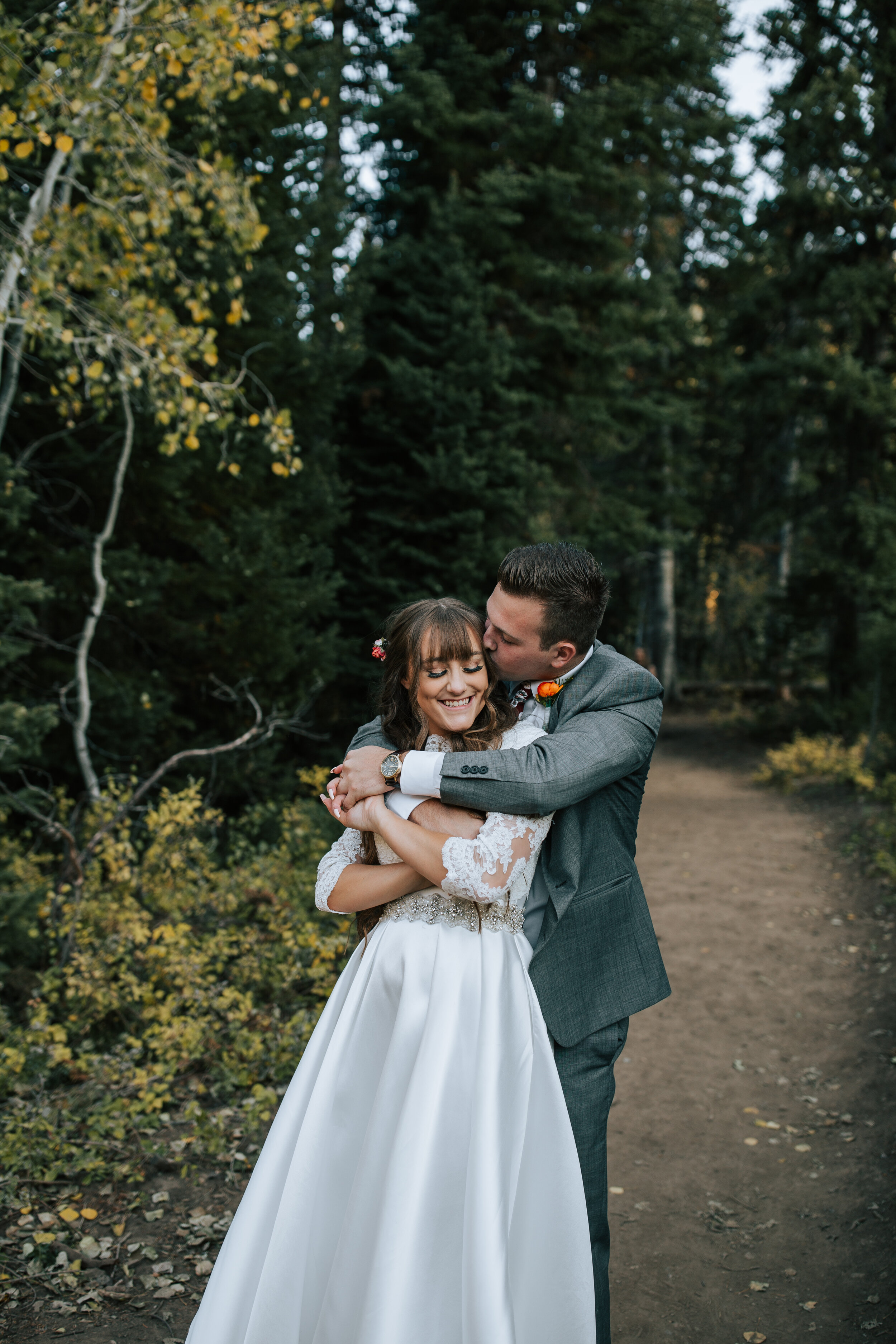  A groom wraps his arms around his bride and kisses the side of her head in a forest in Utah by Emily Jenkins Photography. cute bridal pictures mountain wedding pictures three quarter length wedding dress sleeve #emilyjenkinsphotography #emilyjenkins