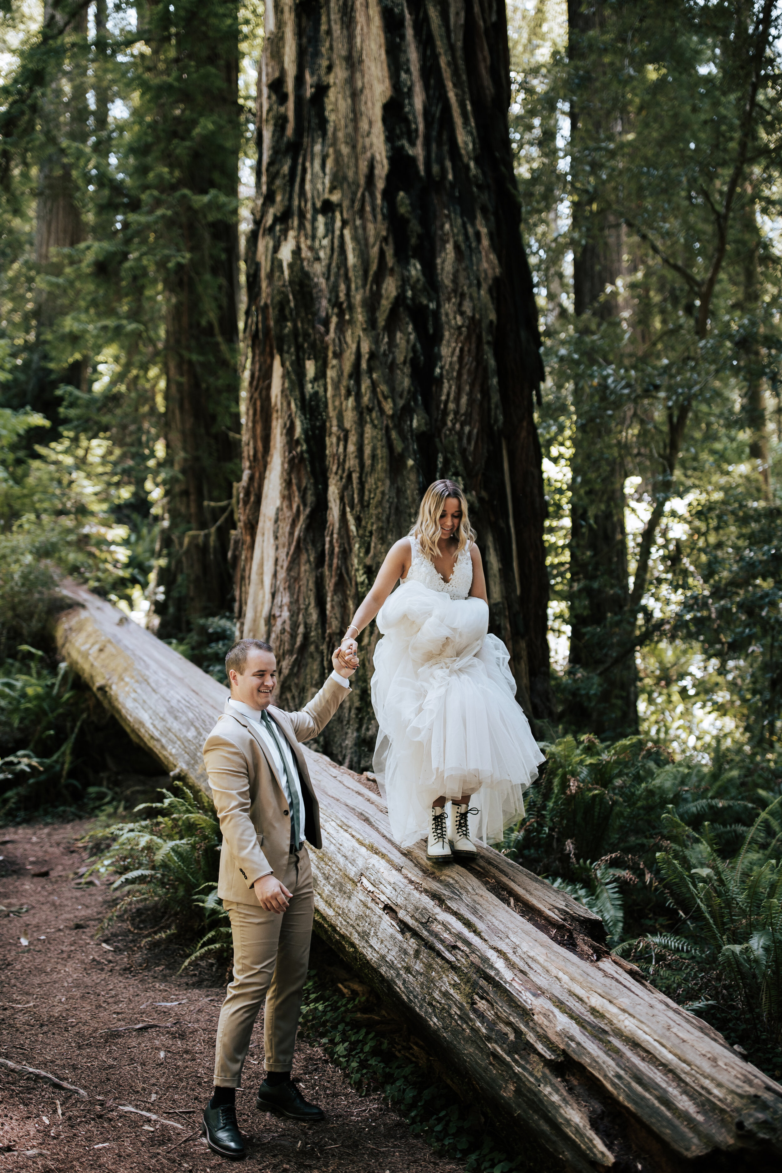  In the Northern California Mountains Emily Jenkins Photography captures a groom helping his bride walk on a large tree during an elopement. northern California elopement redwood elopement photography wedding boots #emilyjenkinsphotography #emilyjenk