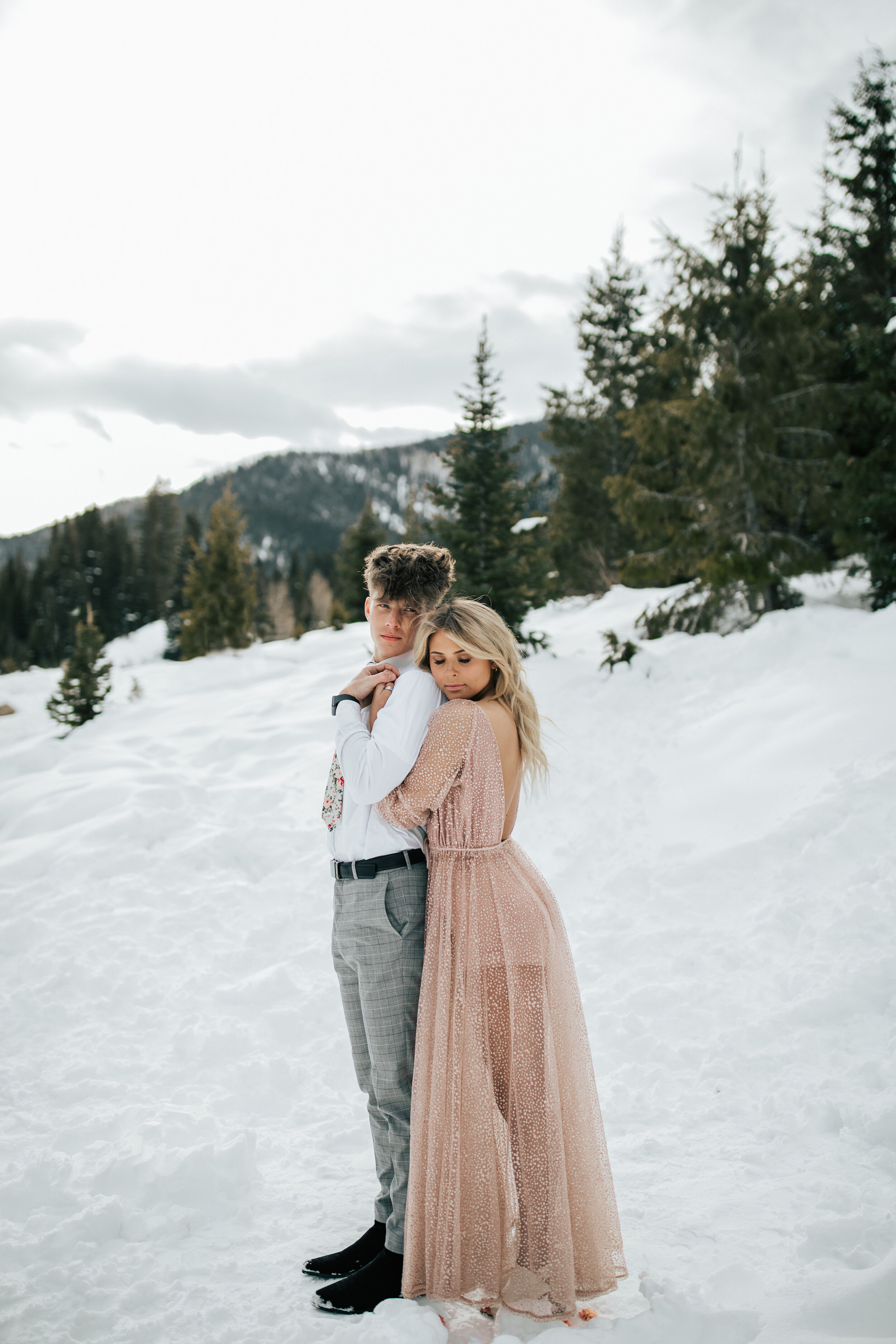  Darling woman snuggles behind her groom in a winter wonderland scene in the Utah Mountains wearing a pink sheer dress by Elopement Photographer Emily Jenkins Photography. snowy bridal photography elopement photographer winter couple photography #emi