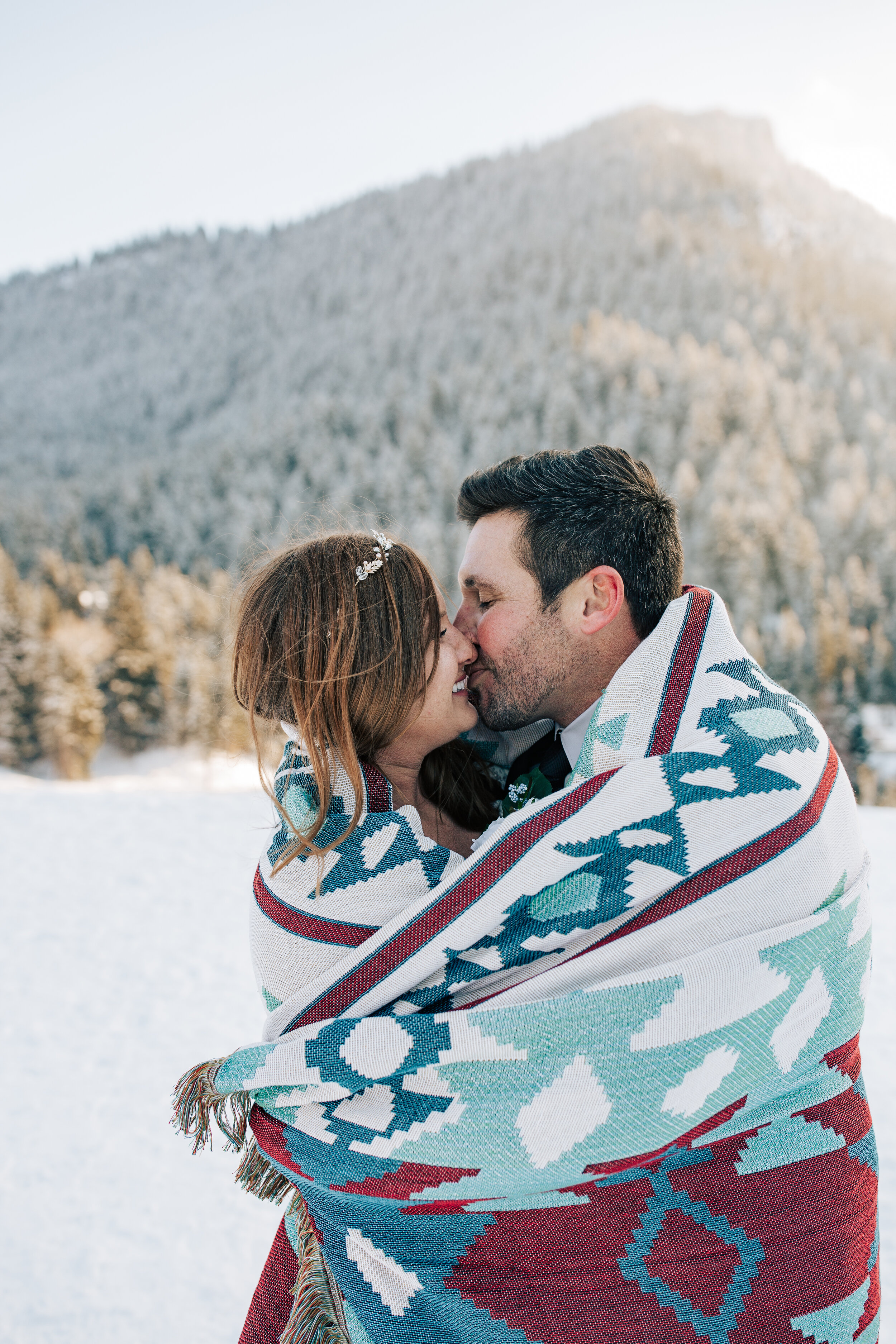  Darling couple snuggle and kiss in a boho blanket in a snowy mountain location captured by West Coast Elopement Photographer Emily Jenkins Photography. kissing while snuggling in a blanket in the snow mountain snow scene bridal pictures #emilyjenkin